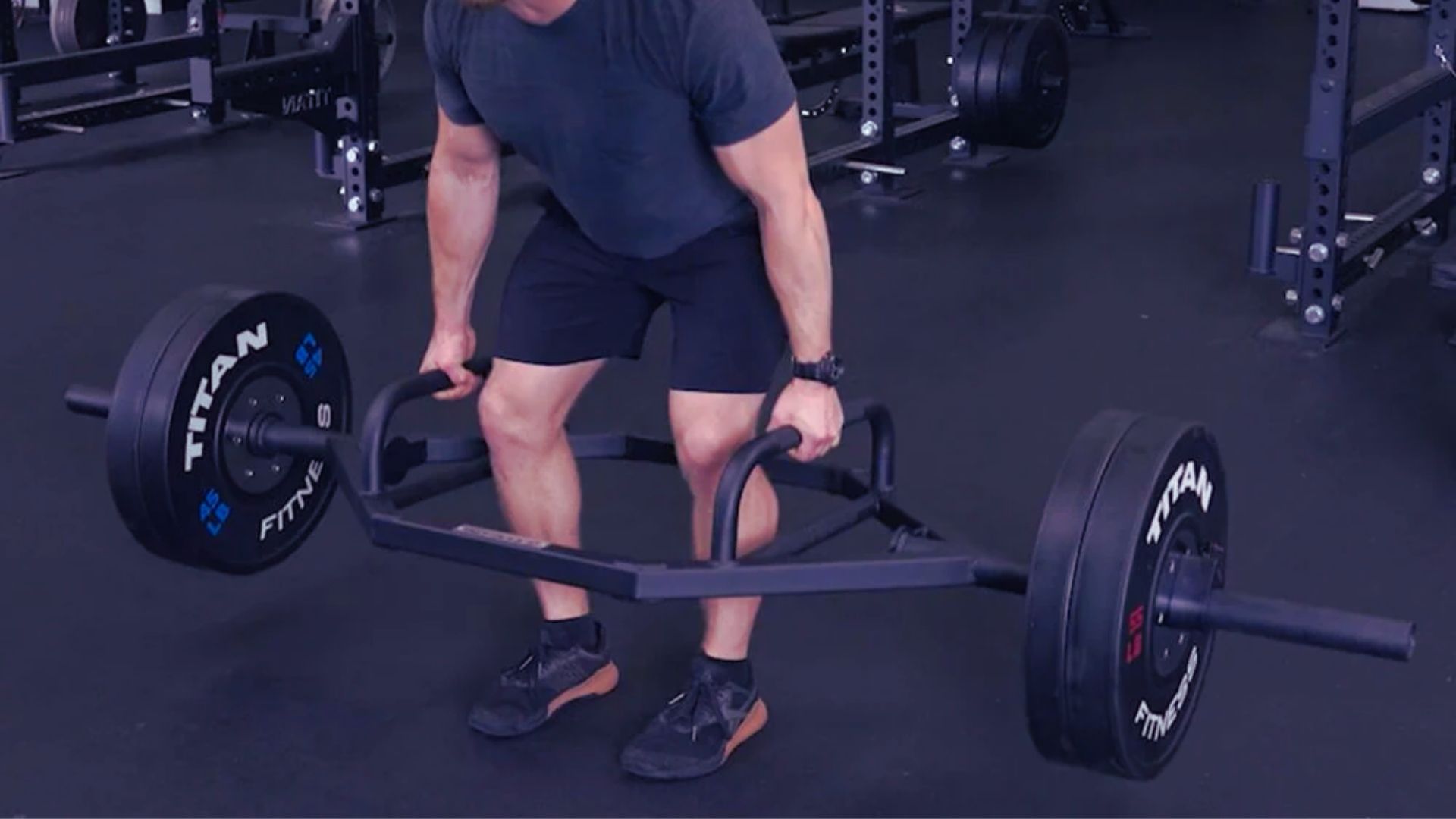 A man lifts a barbell in a gym, using a heavy-duty rackable hex bar for strength training.