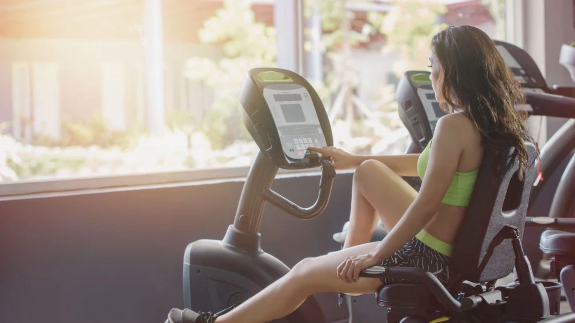 A woman is exercising on a stationary bike in a gym, focused on her workout amidst fitness equipment.