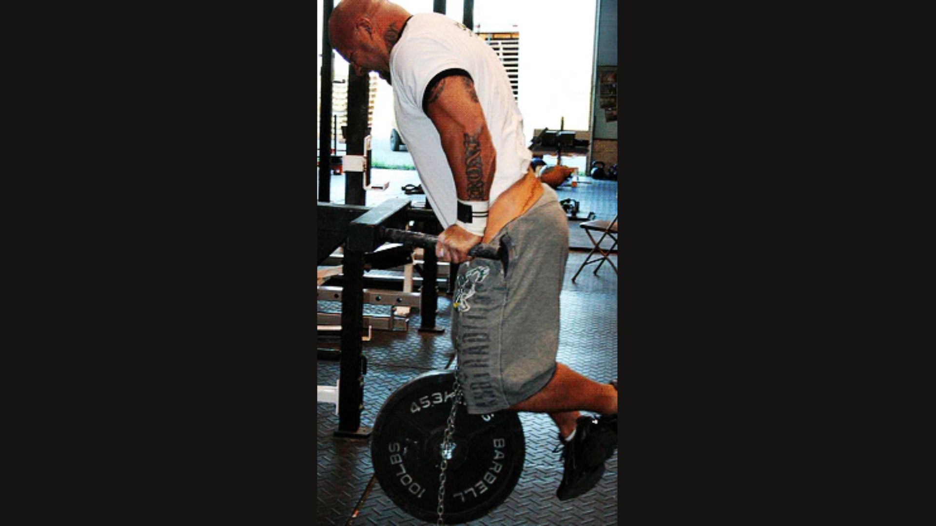 A man performing a pull-up on a barbell, demonstrating strength training for shoulder activation.