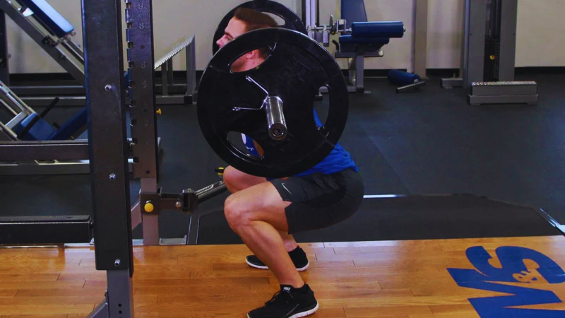 A man performs squats on a hack squat machine in a gym, focusing on his form and strength training.