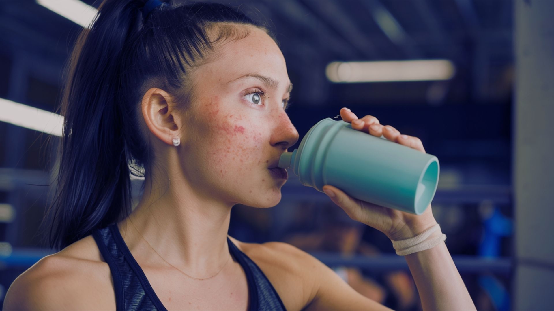 A woman sips from a green shaker, emphasizing her pre-workout connection and addressing acne concerns.