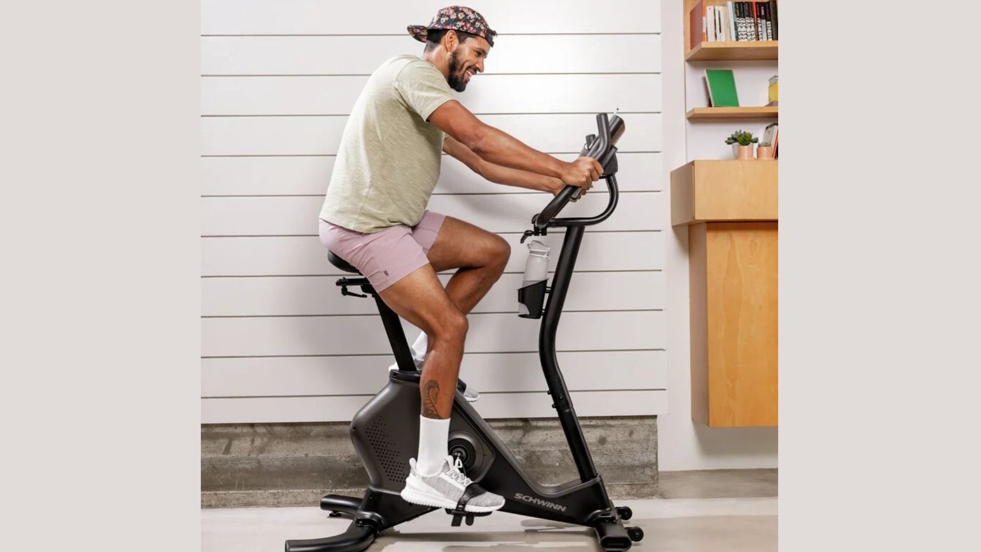 A man is exercising on a stationary bike in a well-lit room, focused on his workout.