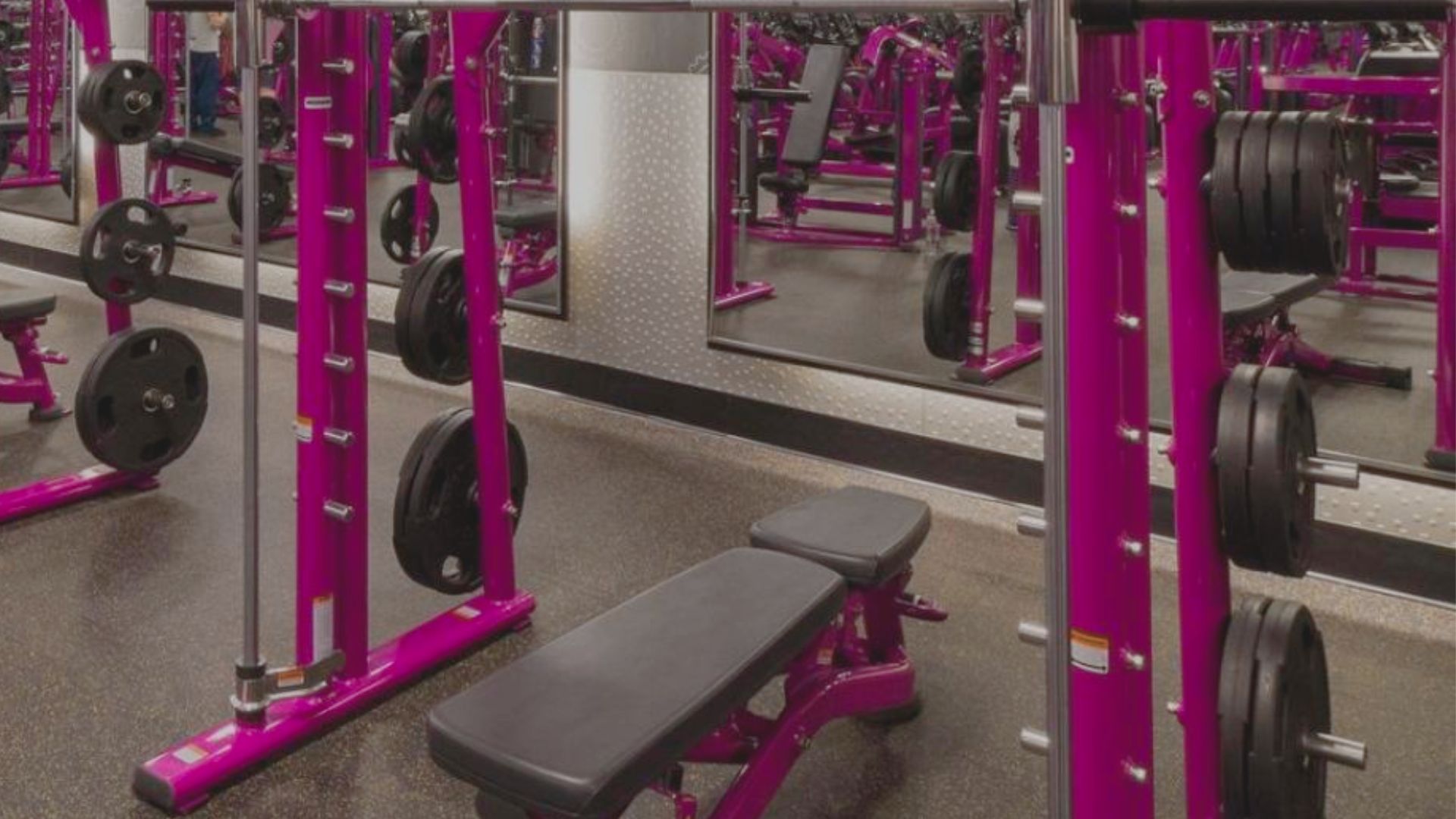 A gym featuring a pink workout smith machine and large mirrors reflecting the vibrant interior.