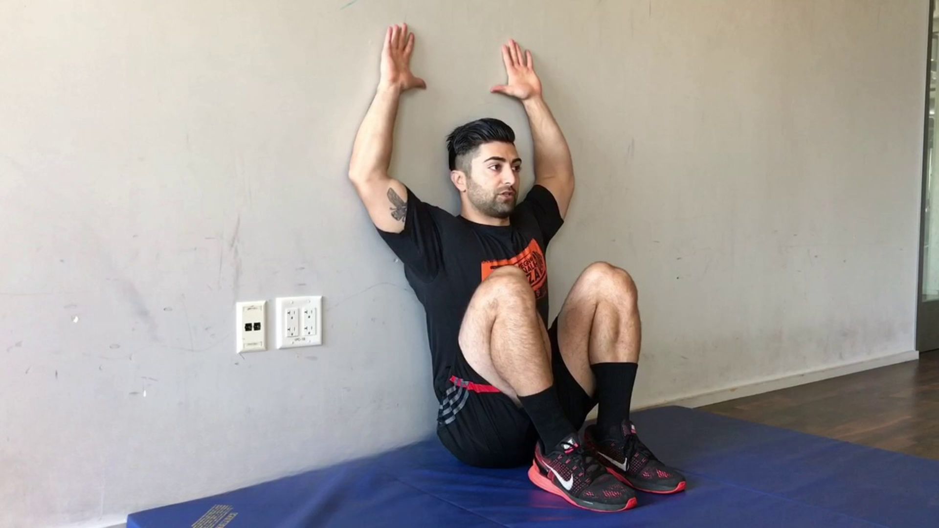 A man performing a wall angel exercise against a wall, demonstrating a simple movement to reduce chest tightness and improve posture.