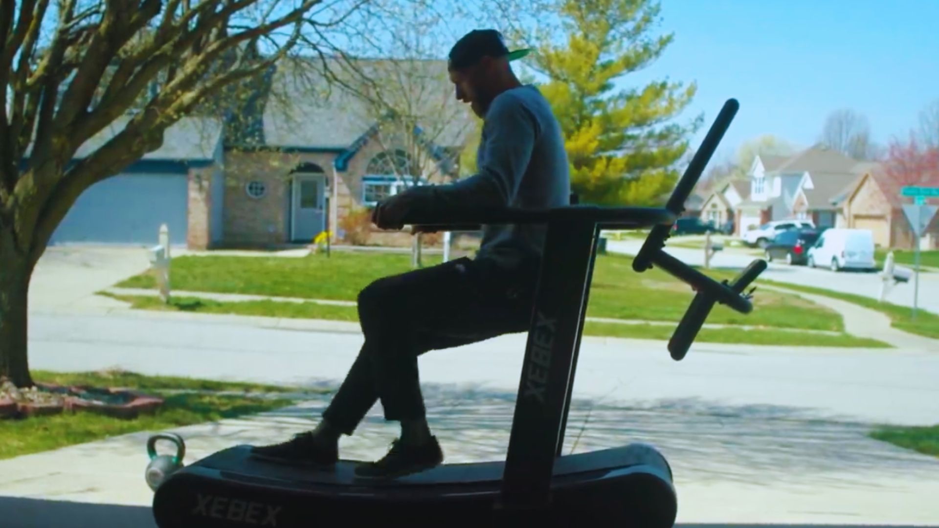 A man rides a stationary bike in front of a house, focusing on his workout in a residential setting.