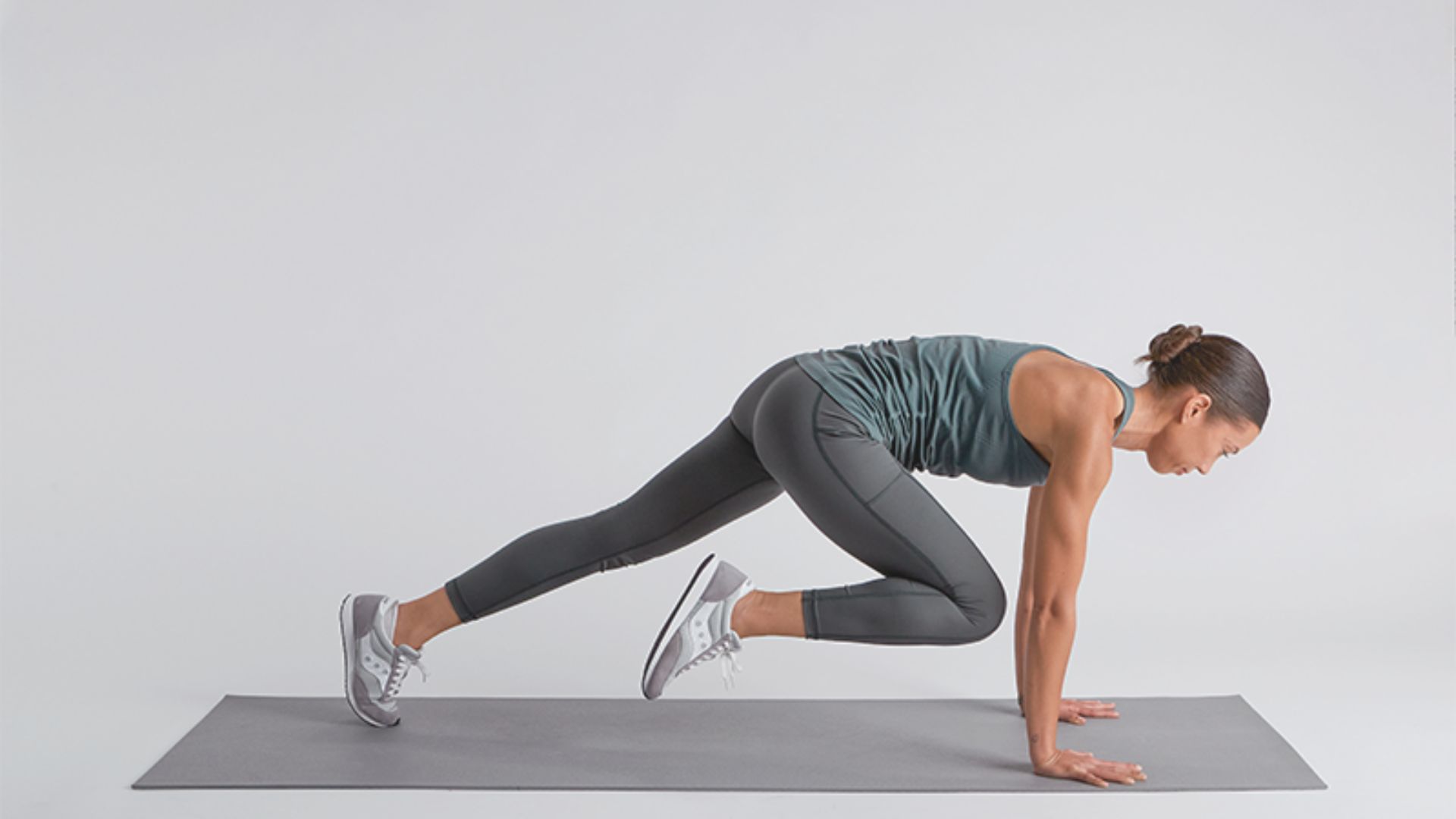 A woman performs a plank exercise on a gray mat, focusing on her core strength and stability.