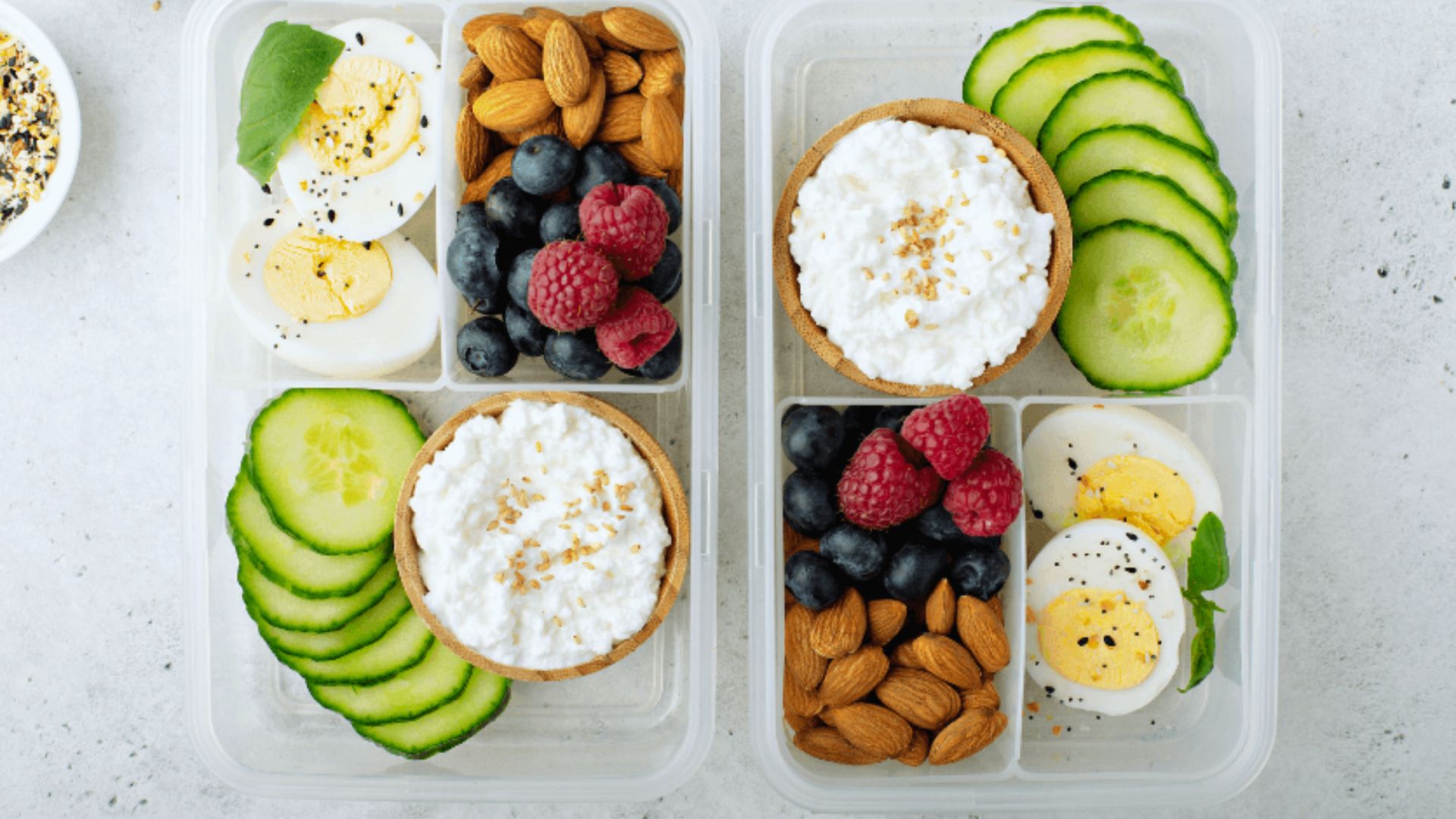 Two food containers: one with eggs, cucumbers, and berries; the other with yogurt, berries, and eggs.