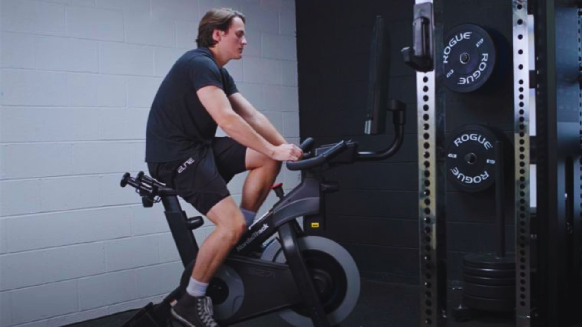 A man is exercising on a stationary bike in a gym setting, focused on his workout.