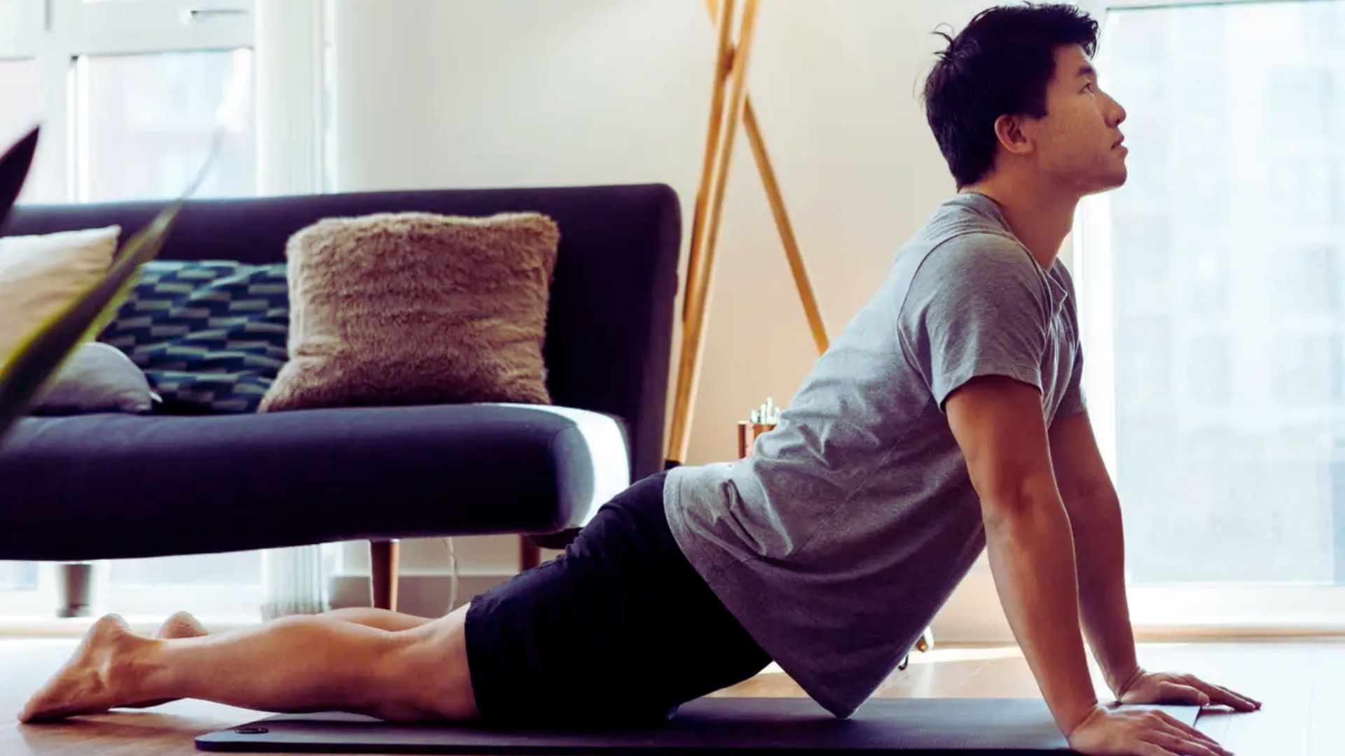 A man performs a yoga pose in a living room, with a couch visible in the background.