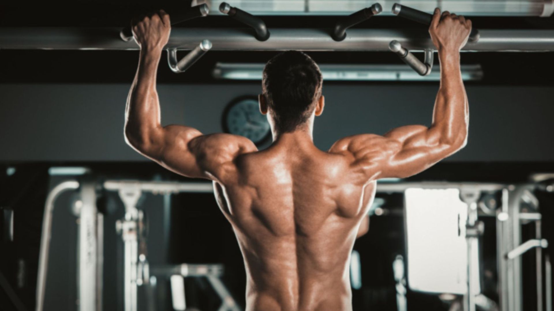 A man performs pull-ups in a gym, focusing on strengthening his latissimus dorsi muscles.