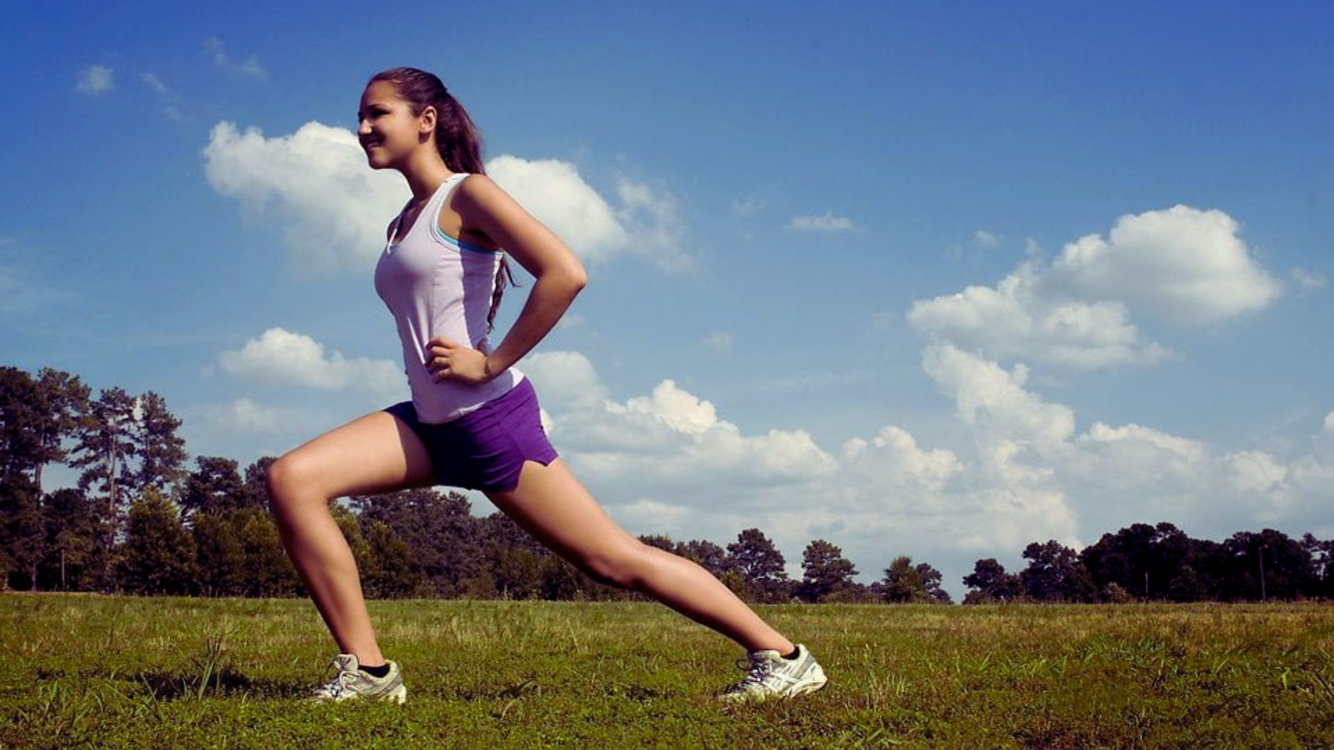 A woman runs through green grass under a bright sun, enjoying a warm and vibrant day outdoors.