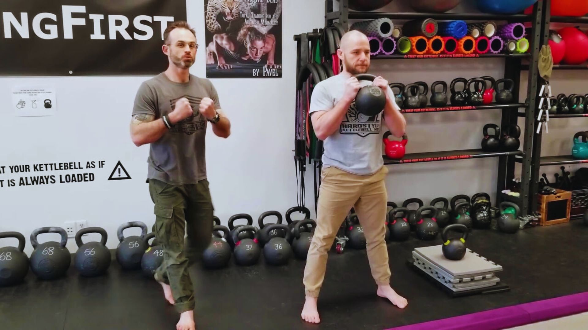 Two men engaged in a kettlebell workout in a gym, demonstrating strength and fitness.