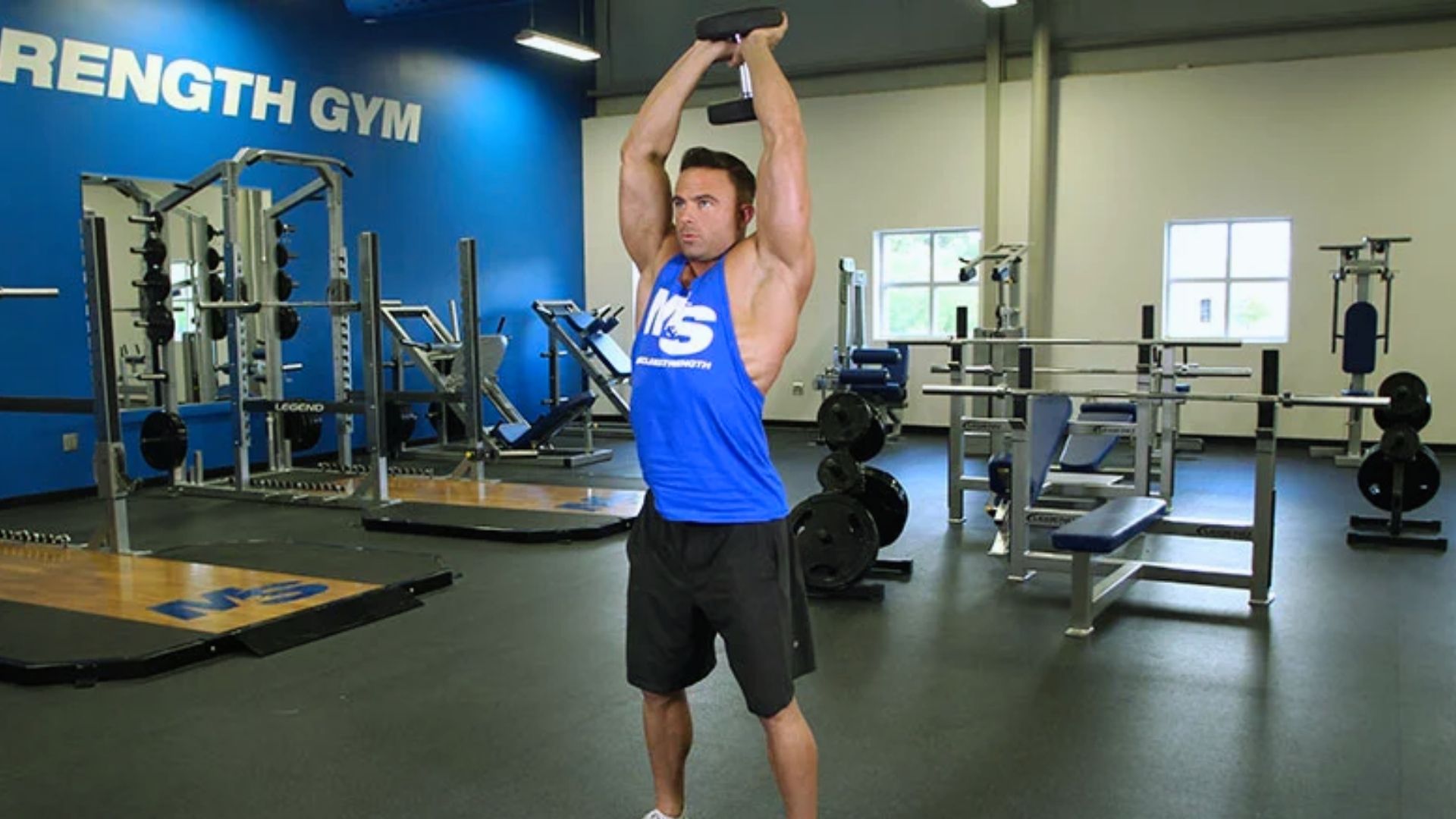 A man performs a dumbbell exercise in a gym, focusing on strength training with weights.