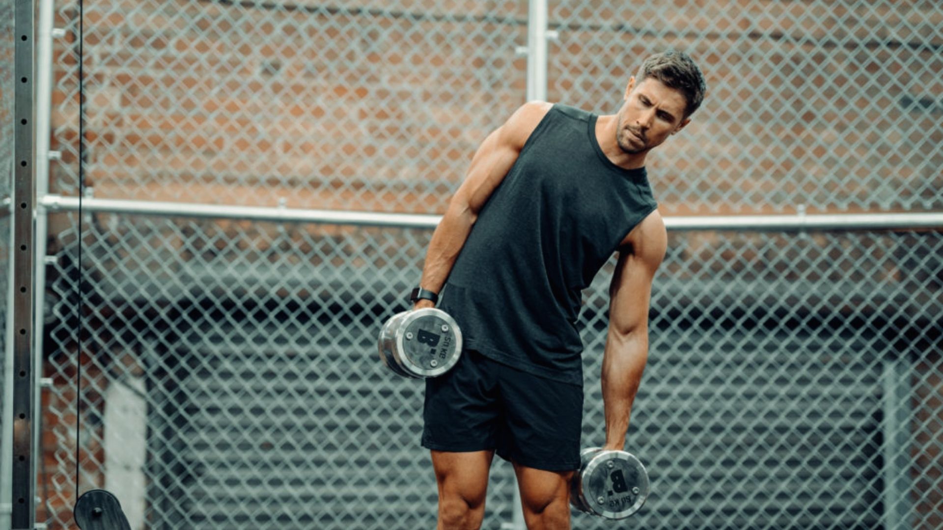 A man holds two dumbbells in each hand, demonstrating strength and fitness in a workout setting.