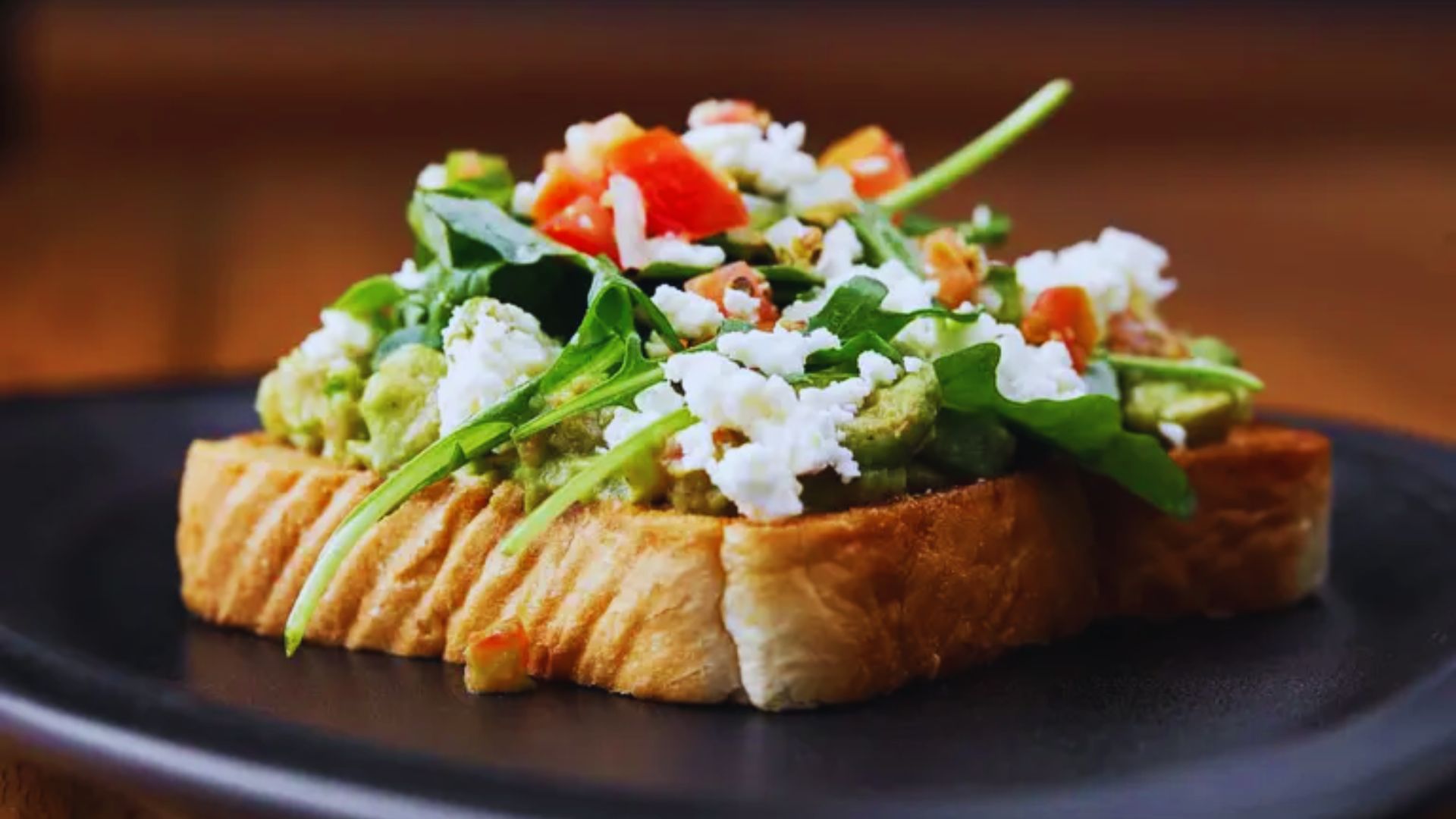 A slice of toast topped with a colorful salad, featuring greens, tomatoes, and cucumbers.