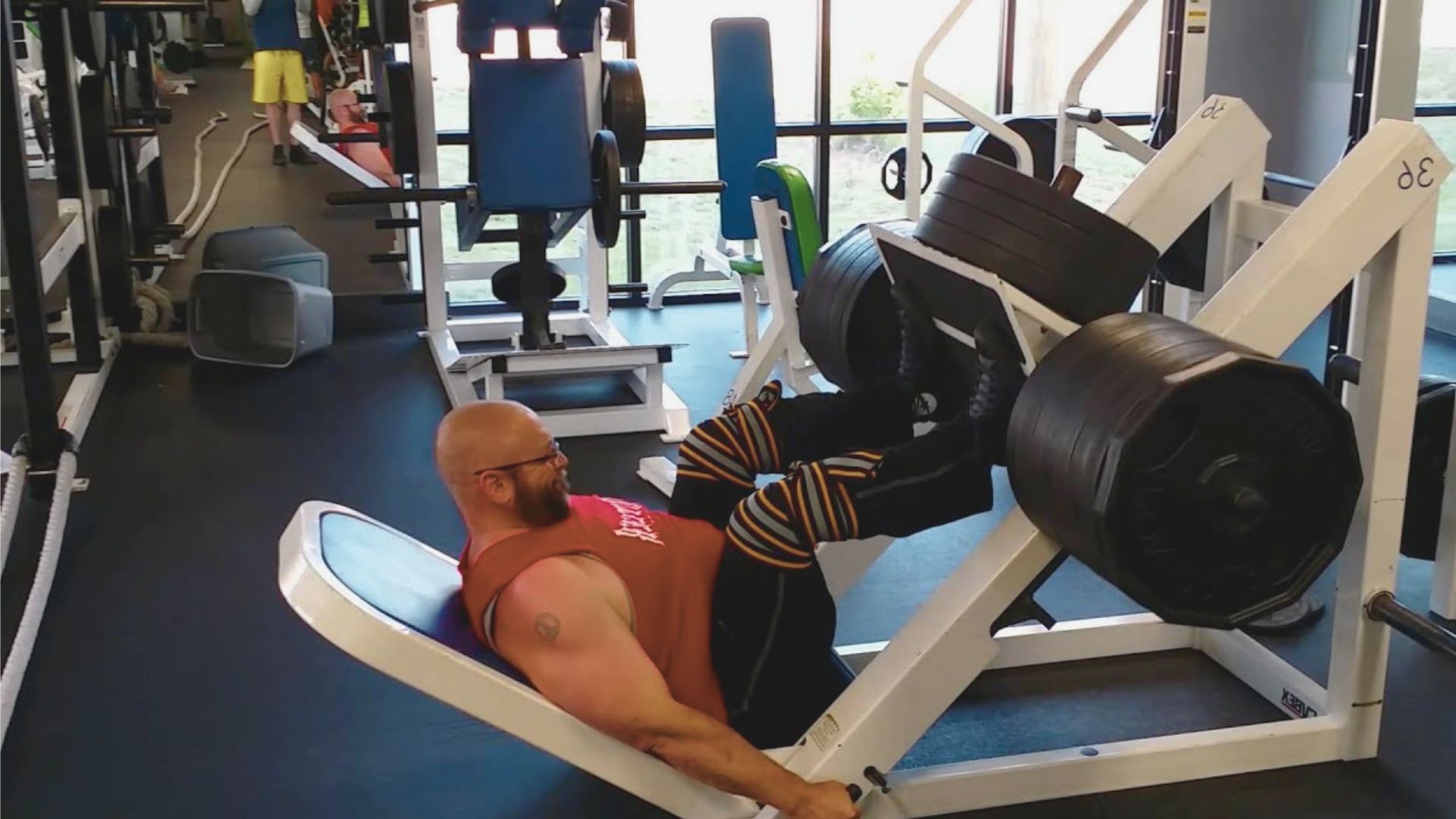 A man performs a leg press exercise in a gym, focusing on strength training with weights on the machine.