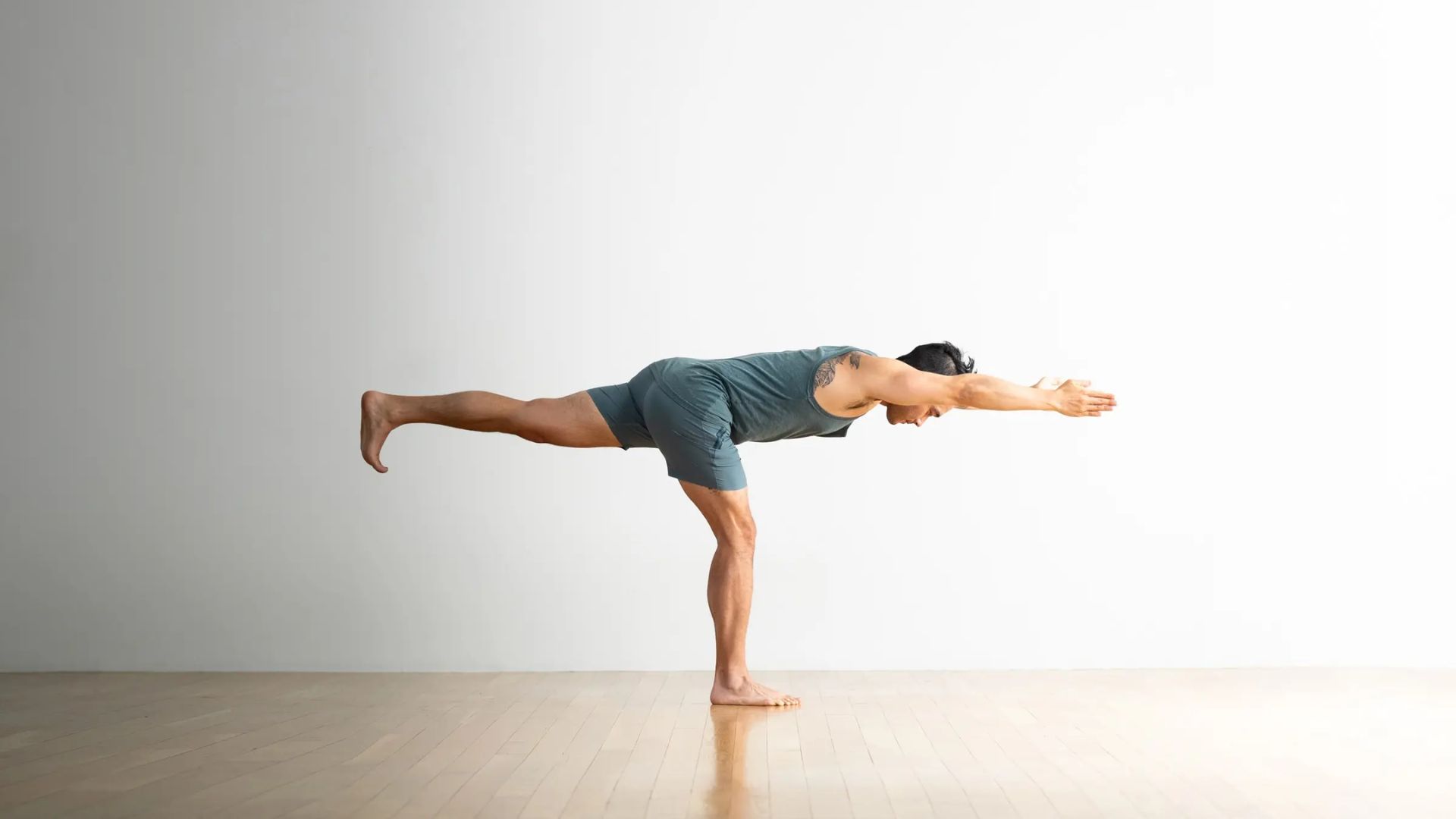A man in a yoga pose on a wooden floor, demonstrating flexibility and mindfulness in a serene environment.