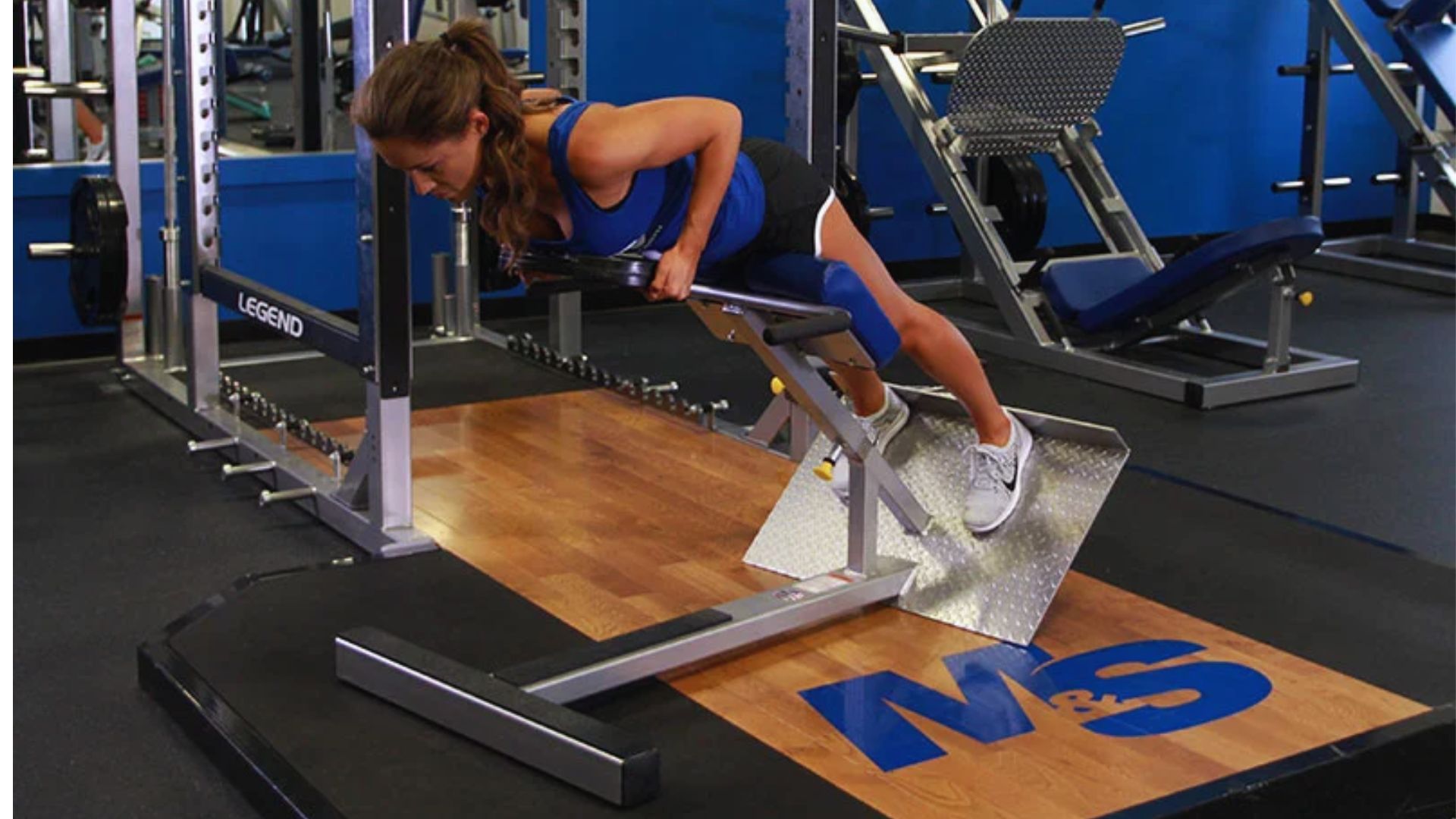A woman performs a pull-up on a weighted hyperextension machine, showcasing strength and focus in her workout.