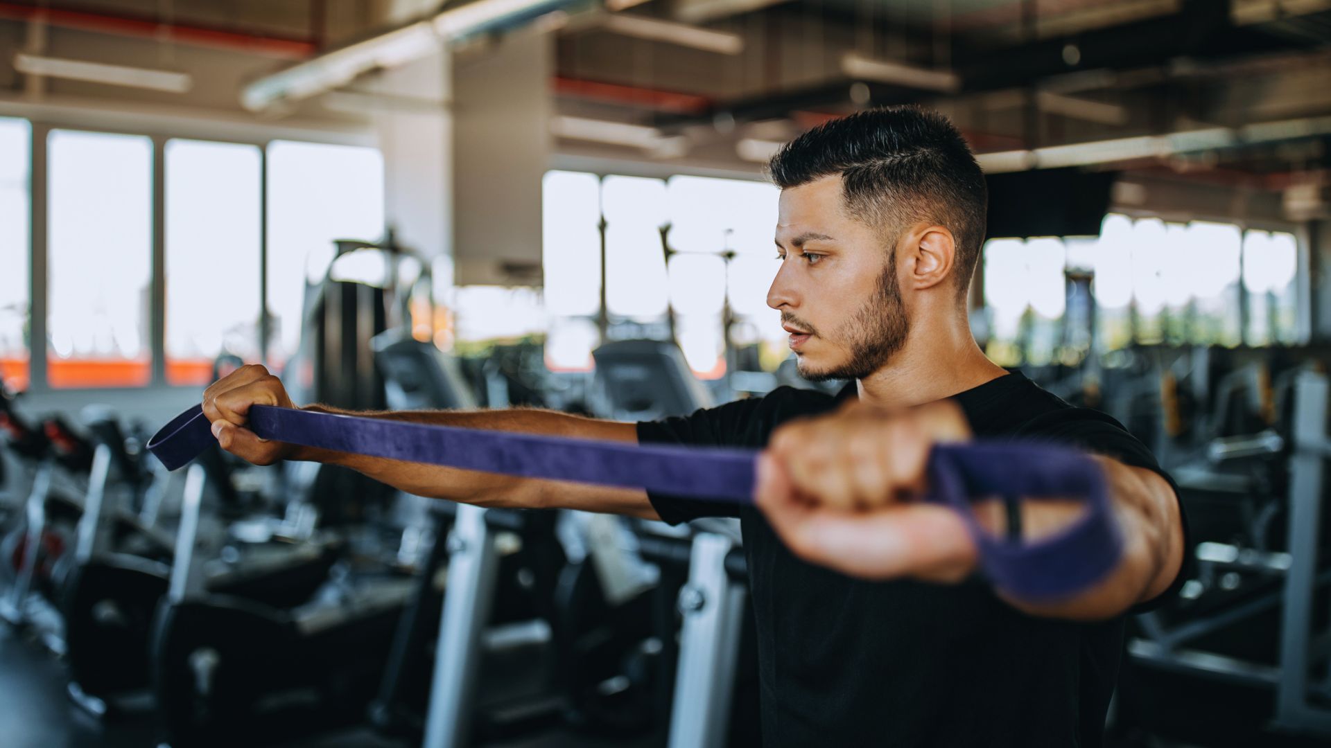 In a gym, a man grips a resistance band, ready to engage in a fitness routine aimed at building muscle.