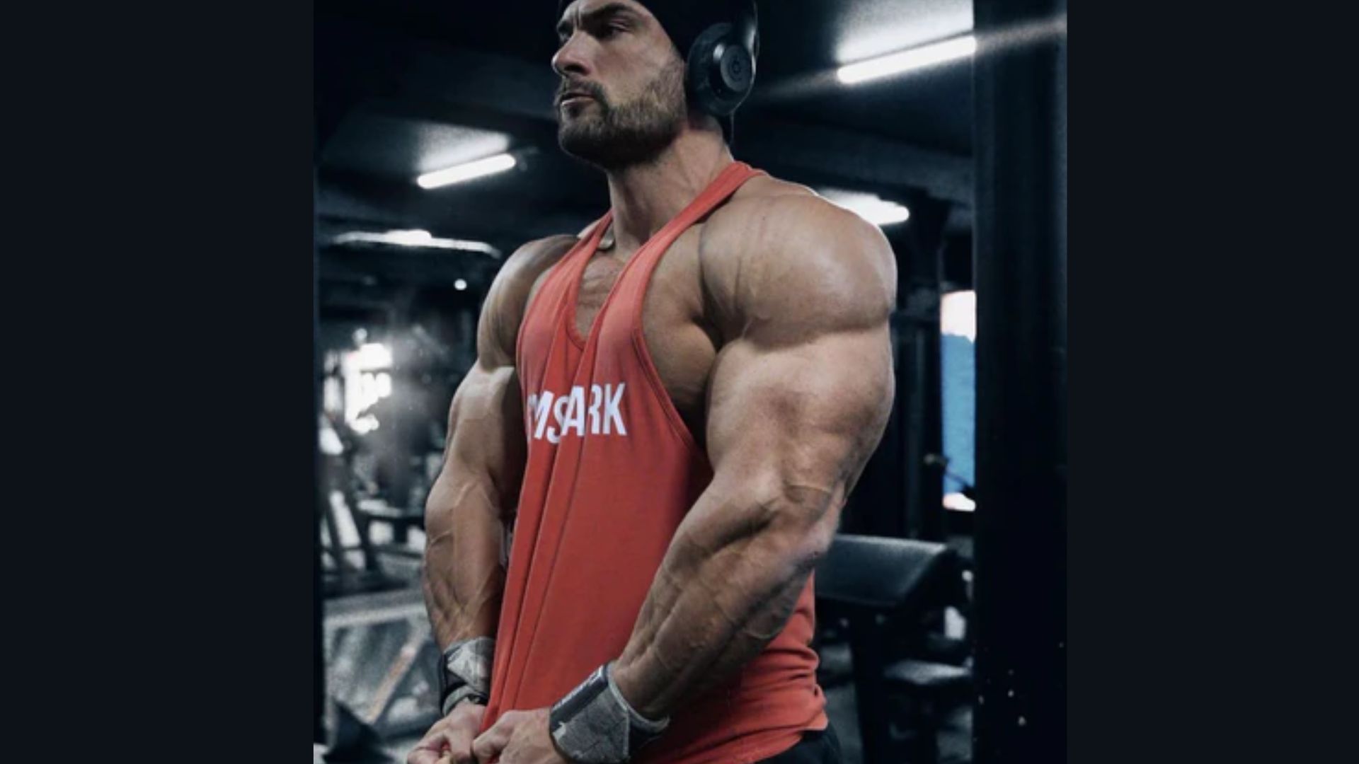 A man in a red tank top stands in a gym, contemplating the relationship between pump duration and muscle growth.