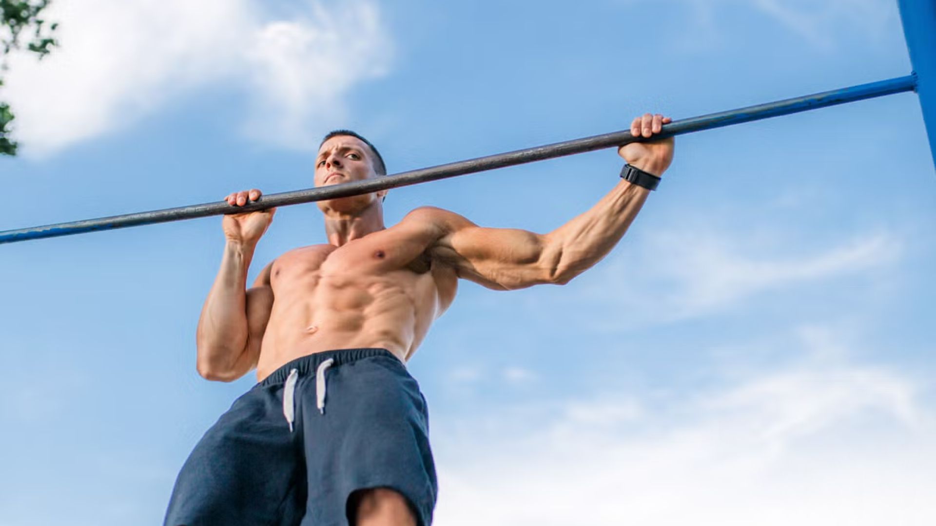 A man performs pull-ups on a horizontal bar, showcasing strength and fitness in an outdoor gym setting.