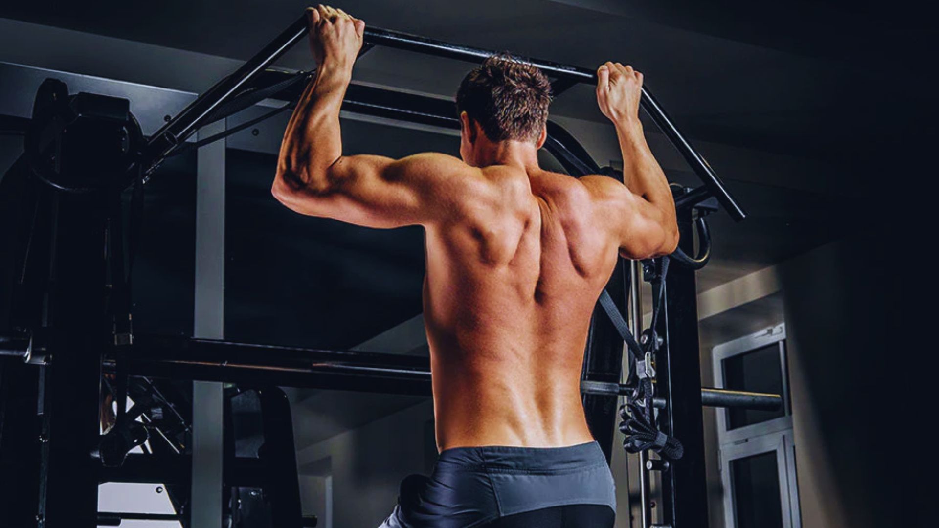A man performs pull-ups on a bar, focusing on his back, traps, and biceps during a pull day workout.