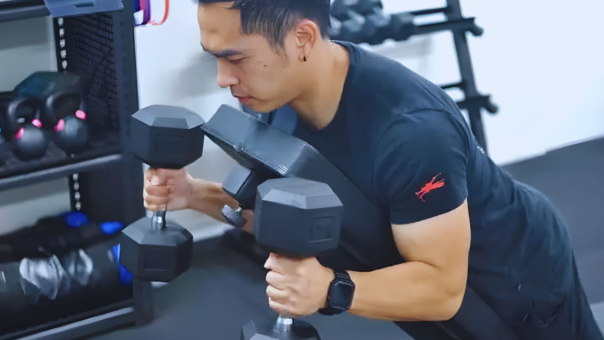 A man is in the starting position for decline hammer curls, holding dumbbells in a gym environment.