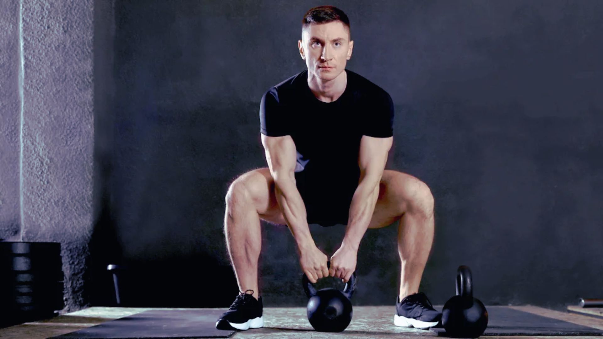 A man performs a squat with kettlebells in a gym, focusing on strength training and fitness.