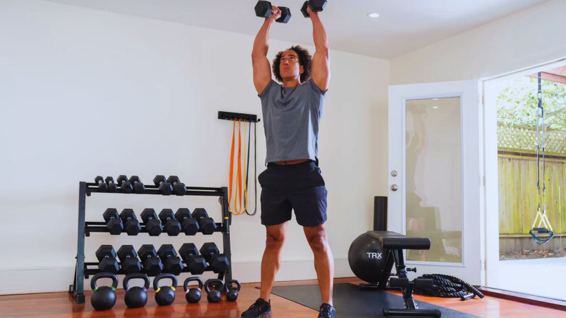 . A man performs a weightlifting exercise in a gym, surrounded by fitness equipment and weights.