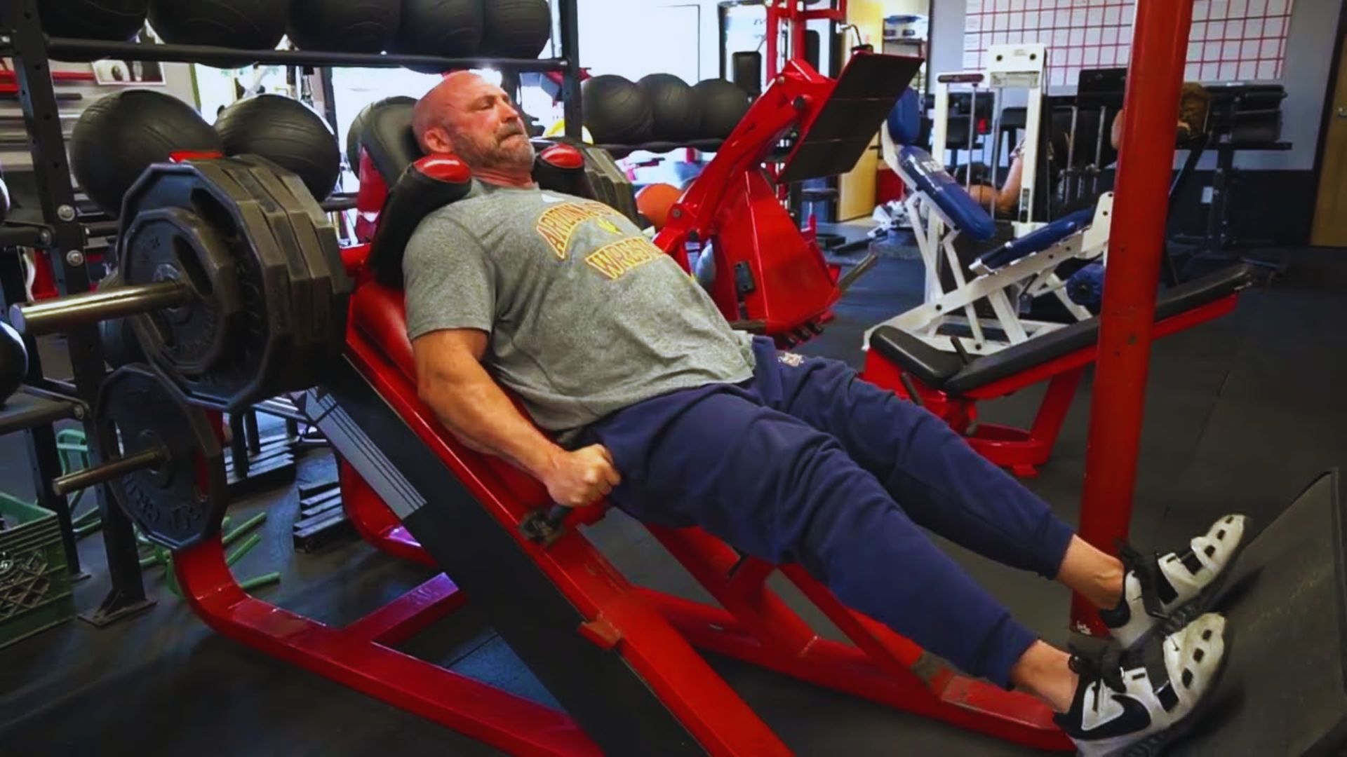 A man is seated on a bench inside a gym, surrounded by exercise equipment.