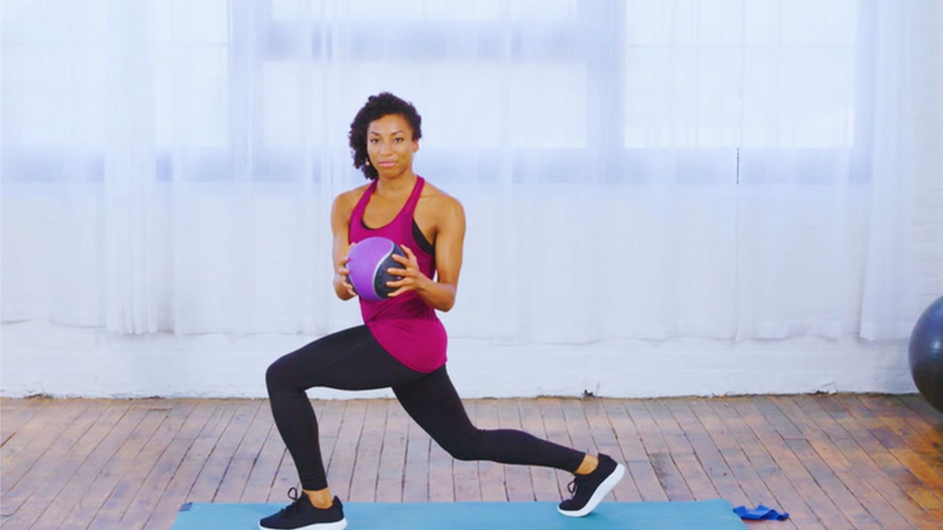 A woman performs a squat while holding a fitness ball, demonstrating strength and balance in her workout routine.