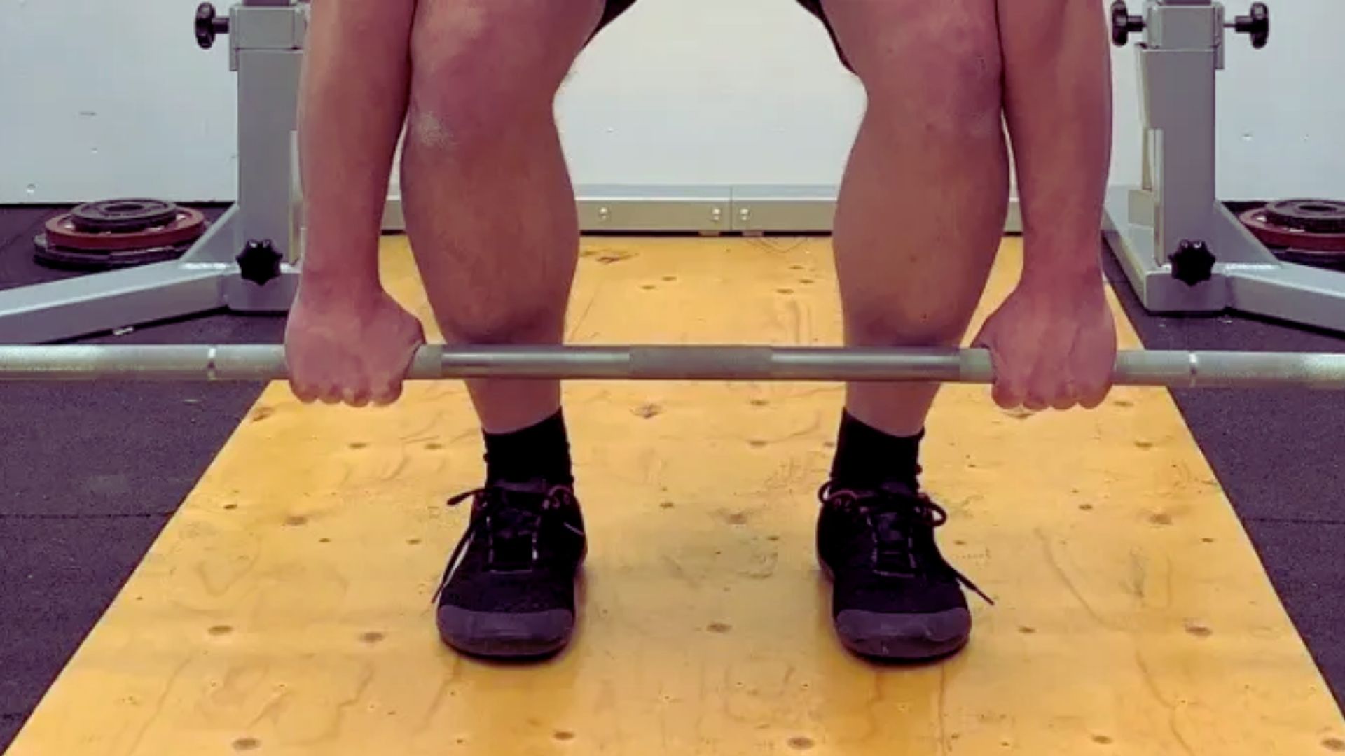 1. A man squats down, preparing to lift a barbell positioned on the ground.