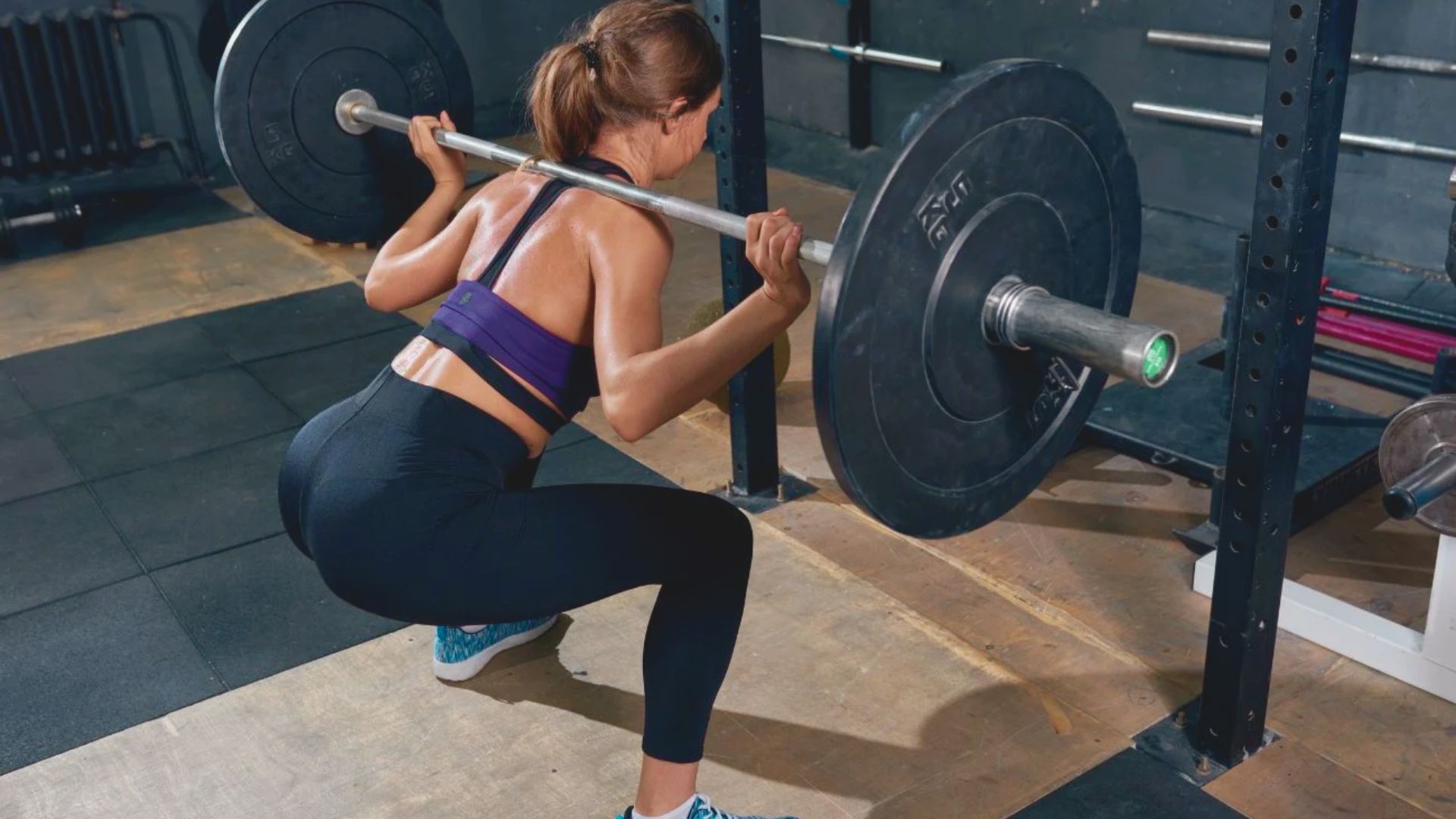 A woman performs a sumo squat with a barbell in a gym, demonstrating proper form and strength training technique.