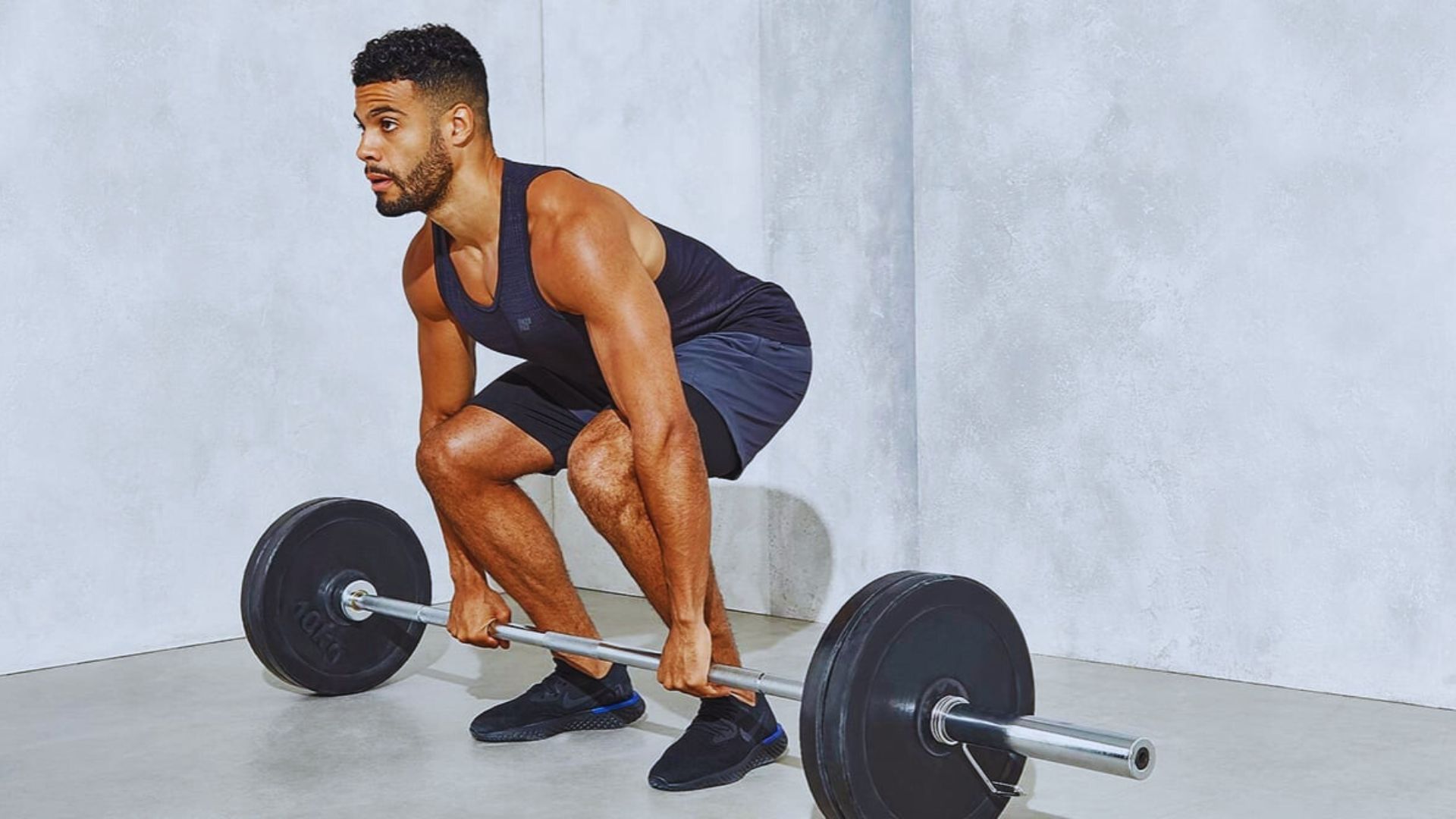 A man deadlift with a barbell and weight, focusing on his form in a gym setting.