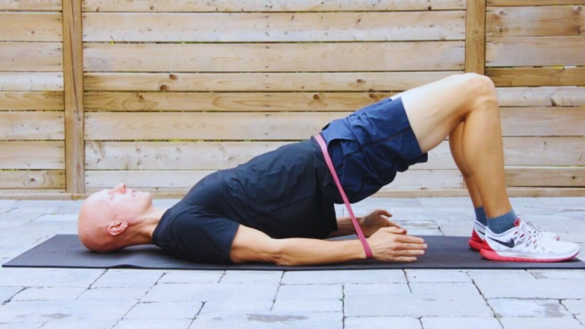 A man performs a side plank exercise while using a pink resistance band for added support and stability.