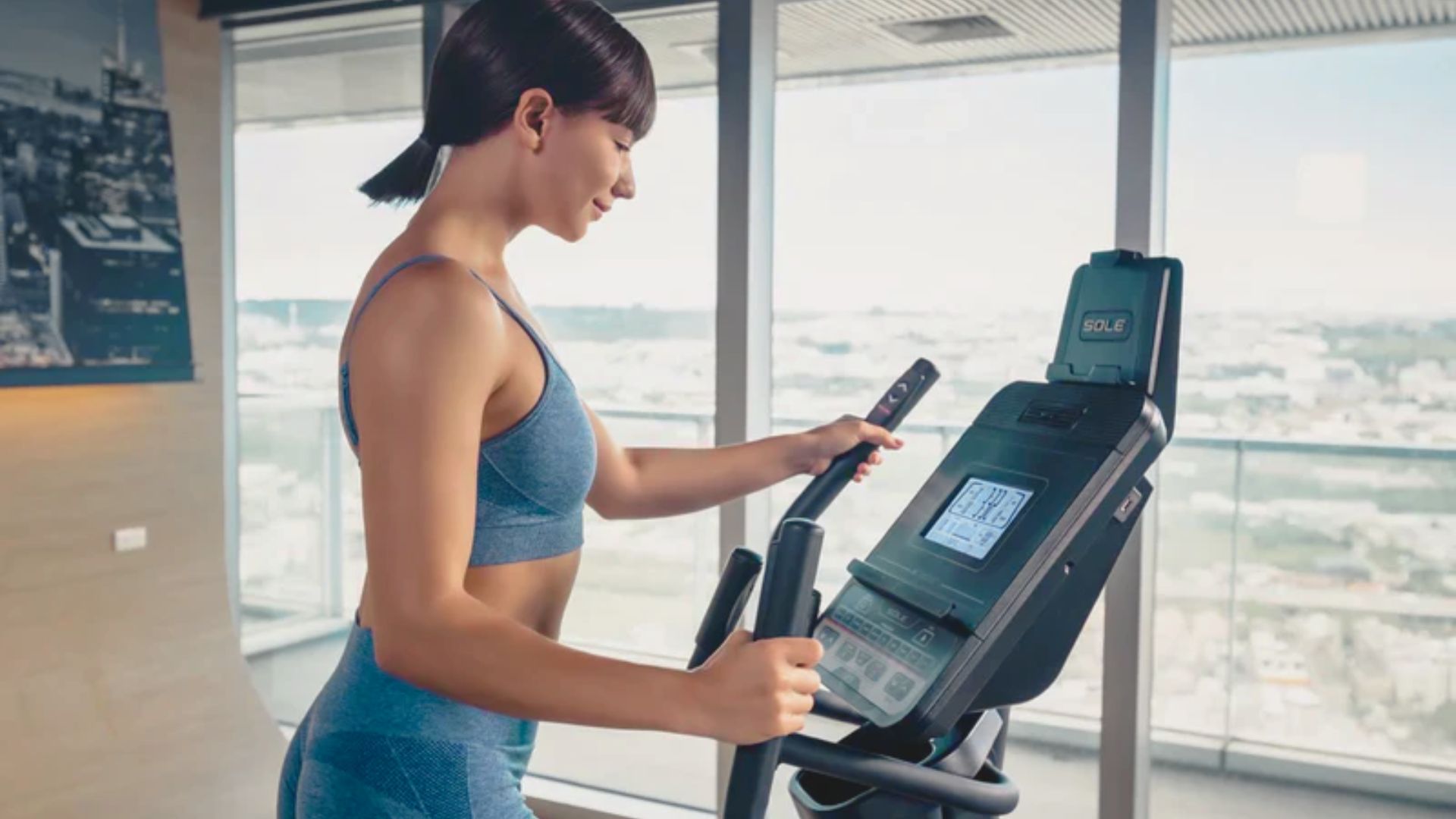 A woman is pedaling on an exercise bike in a gym, focused on her workout amidst various gym equipment.