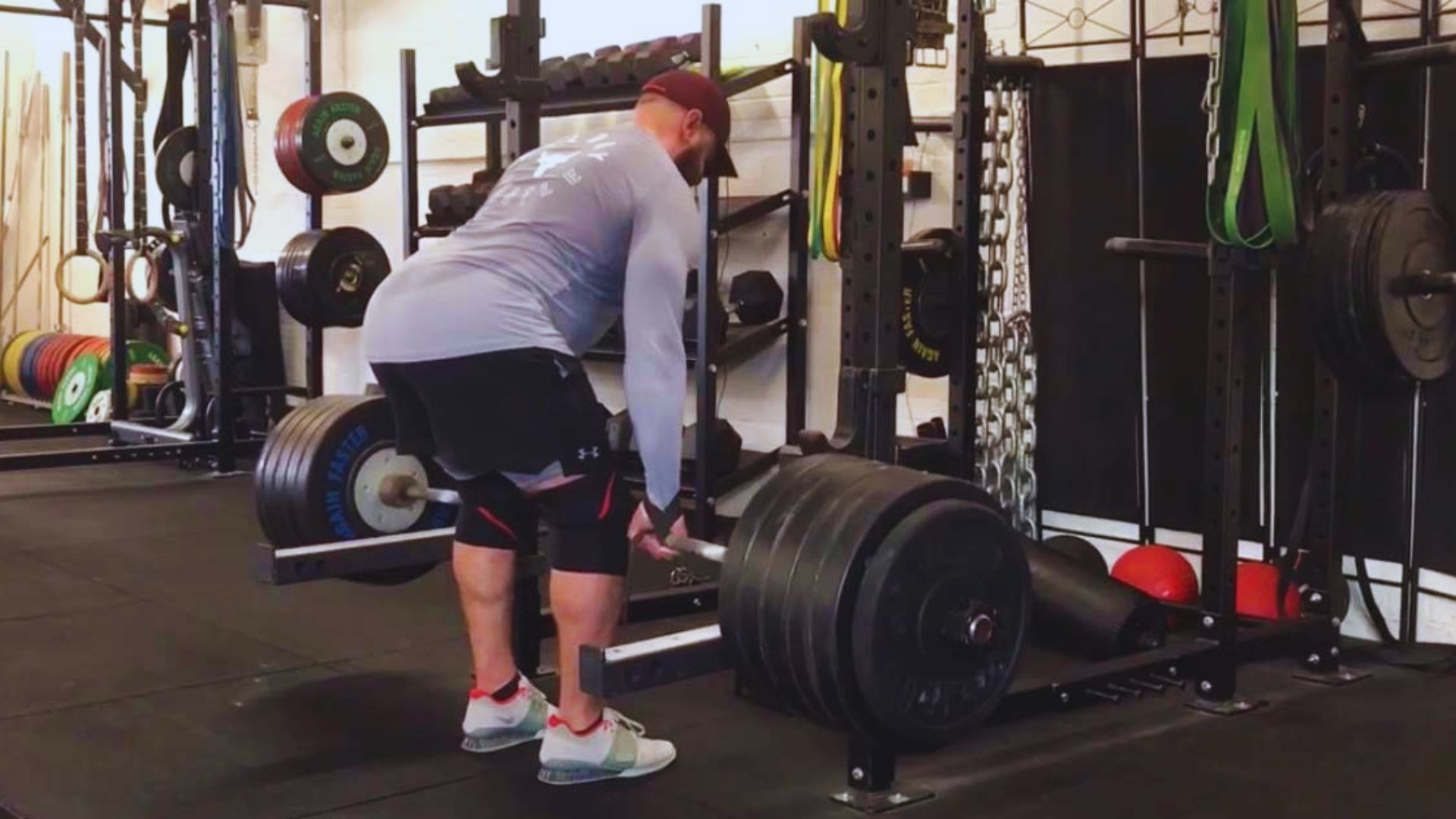 A man squats on a barbell in a gym, demonstrating proper form for Romanian deadlifts targeting the lower back.