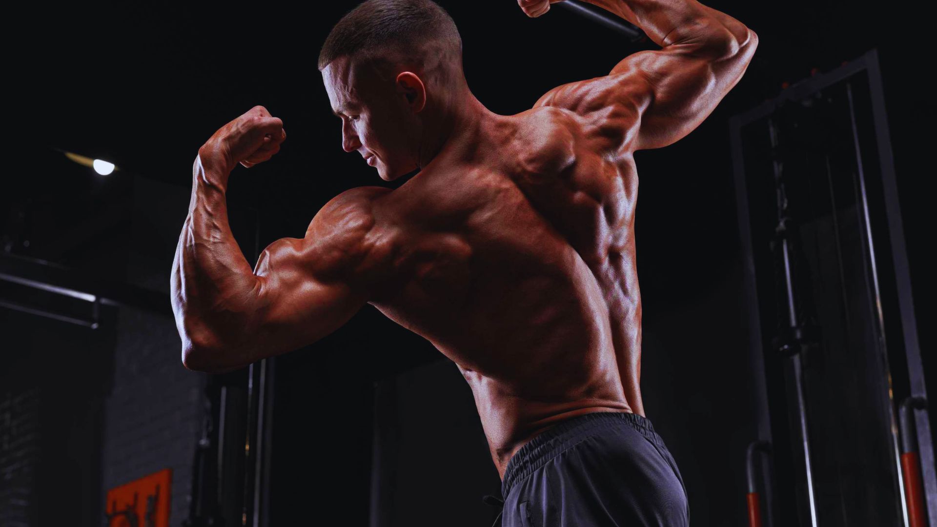 A man flexes his muscles in a gym, showcasing strength and fitness during a workout session.