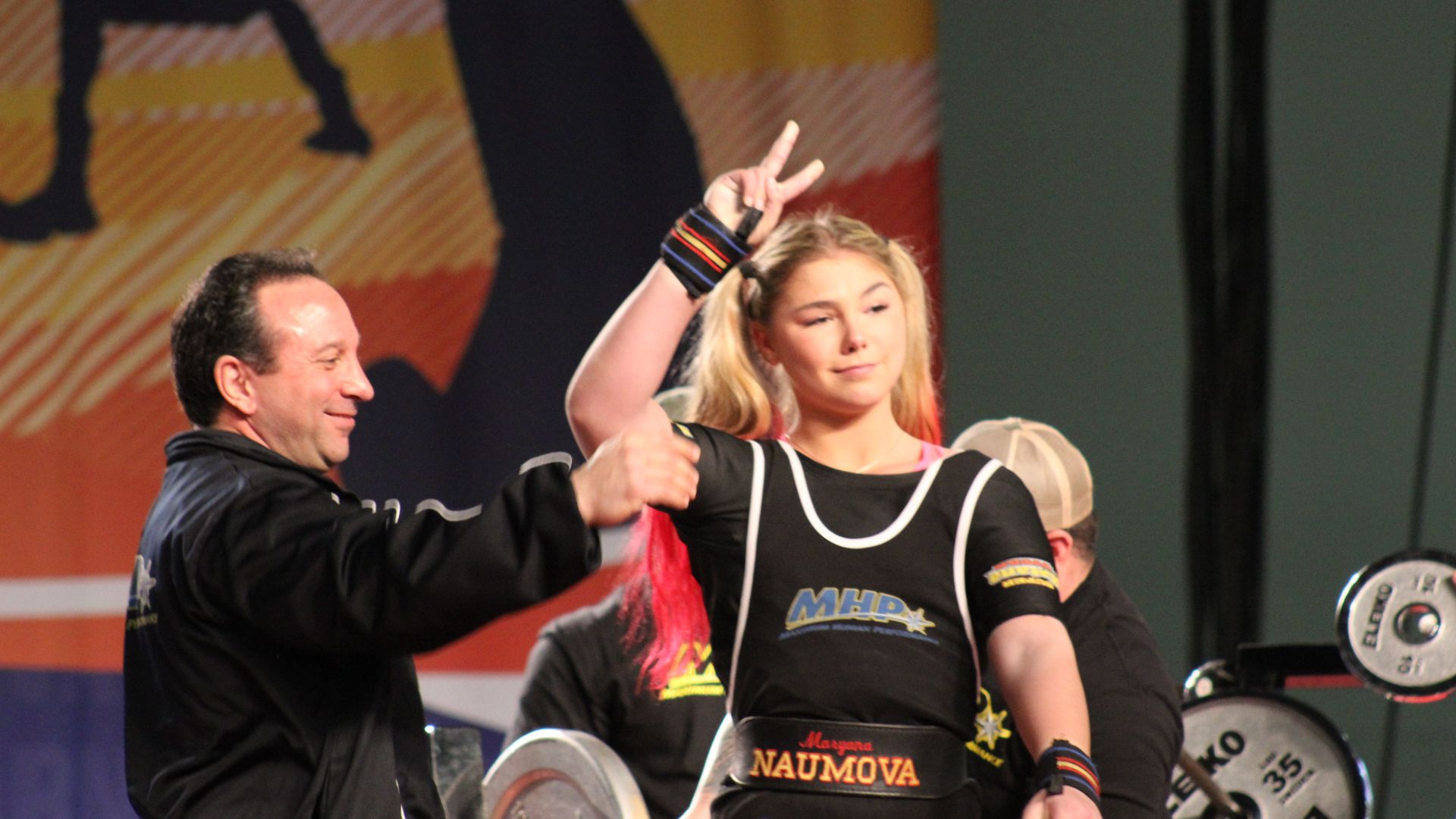 A woman gives a thumbs up to a man, encouraging him in a discussion about age-appropriate bench press performance.