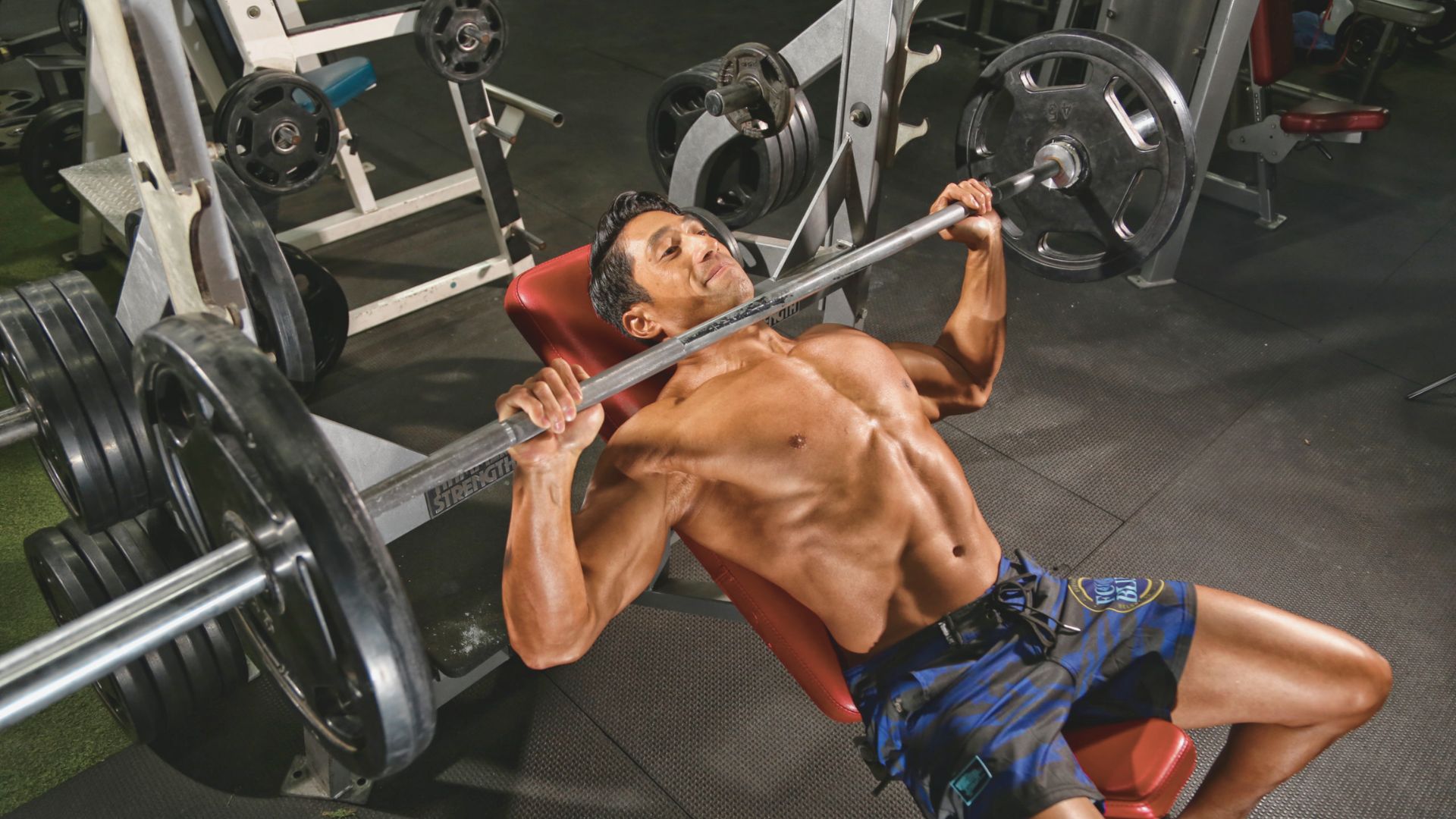 A man performs a bench press in a gym, focusing on his chest, shoulders, and triceps during a push day workout.