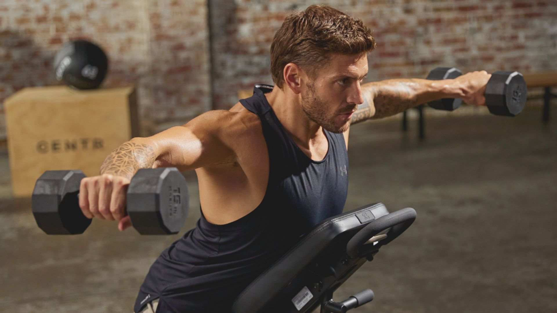 A man performs a dumbbell exercise in a gym, focusing on strength training with weights.