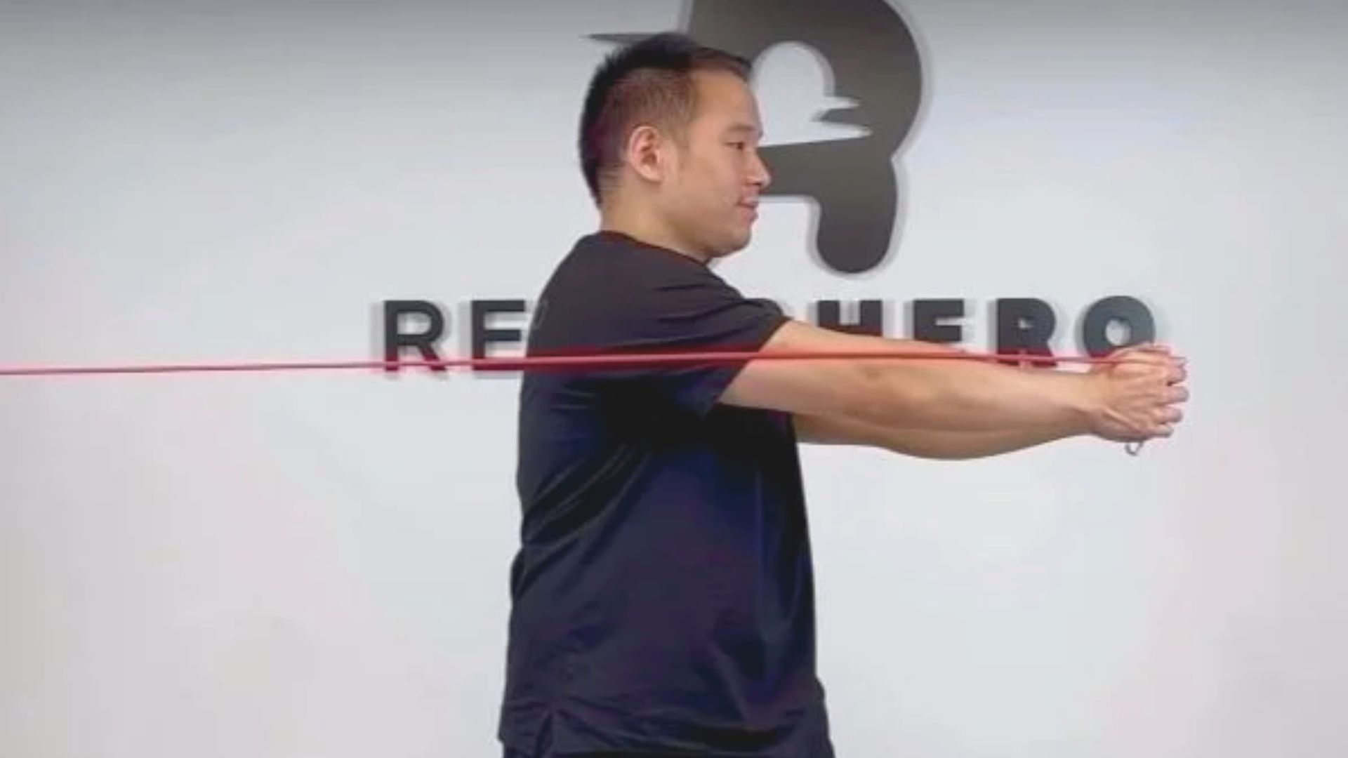 A man stands in front of a wall, holding a red rope in his hands.