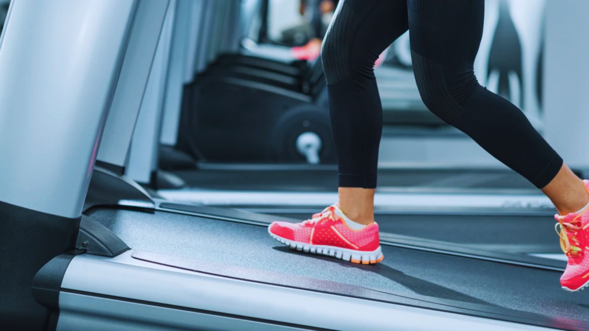 A woman wearing pink sneakers runs on a treadmill in a gym setting, focused on her workout.