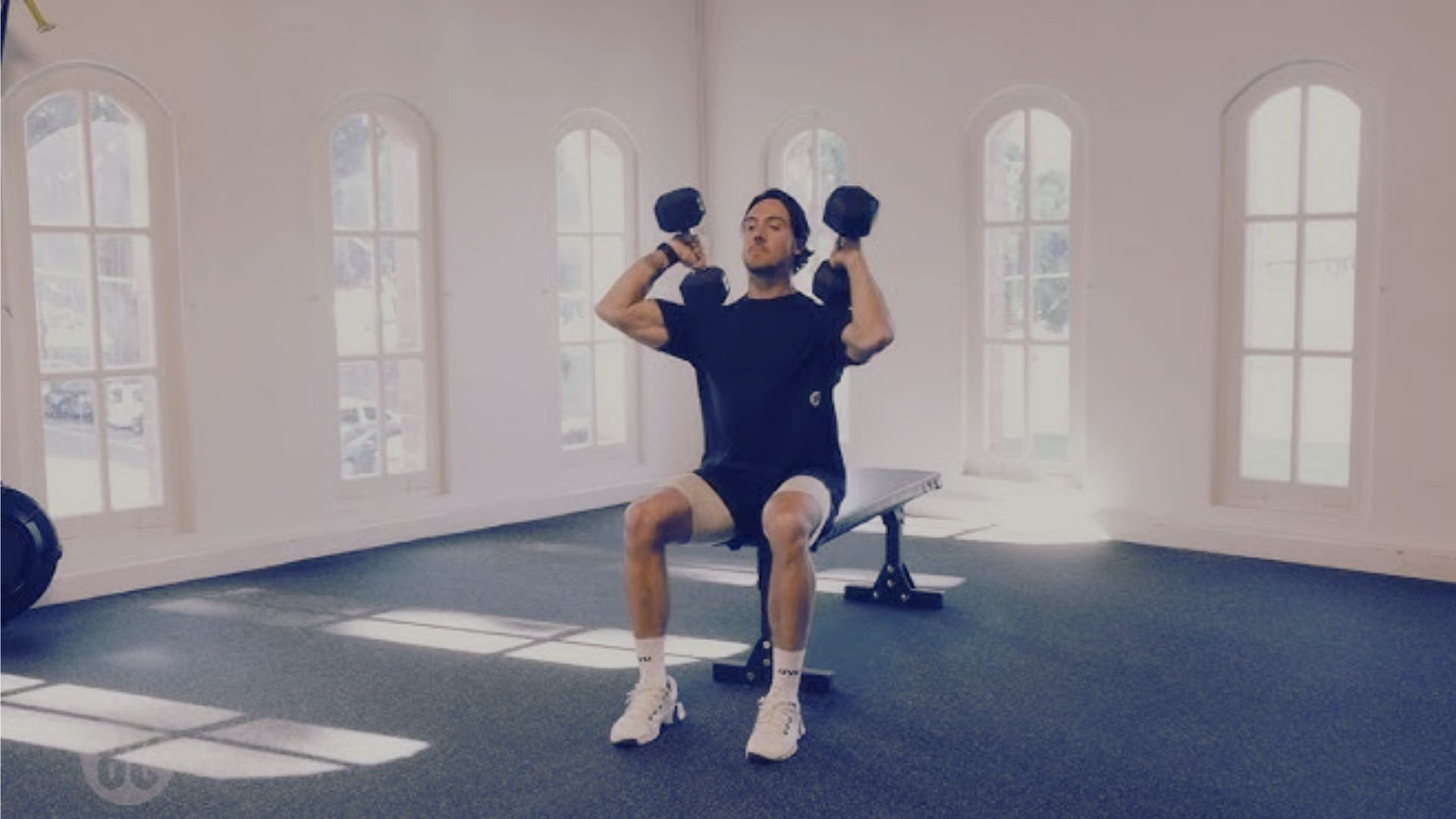 A man performs a seated dumbbell power clean in a gym, focusing on upper body strength and coordination.