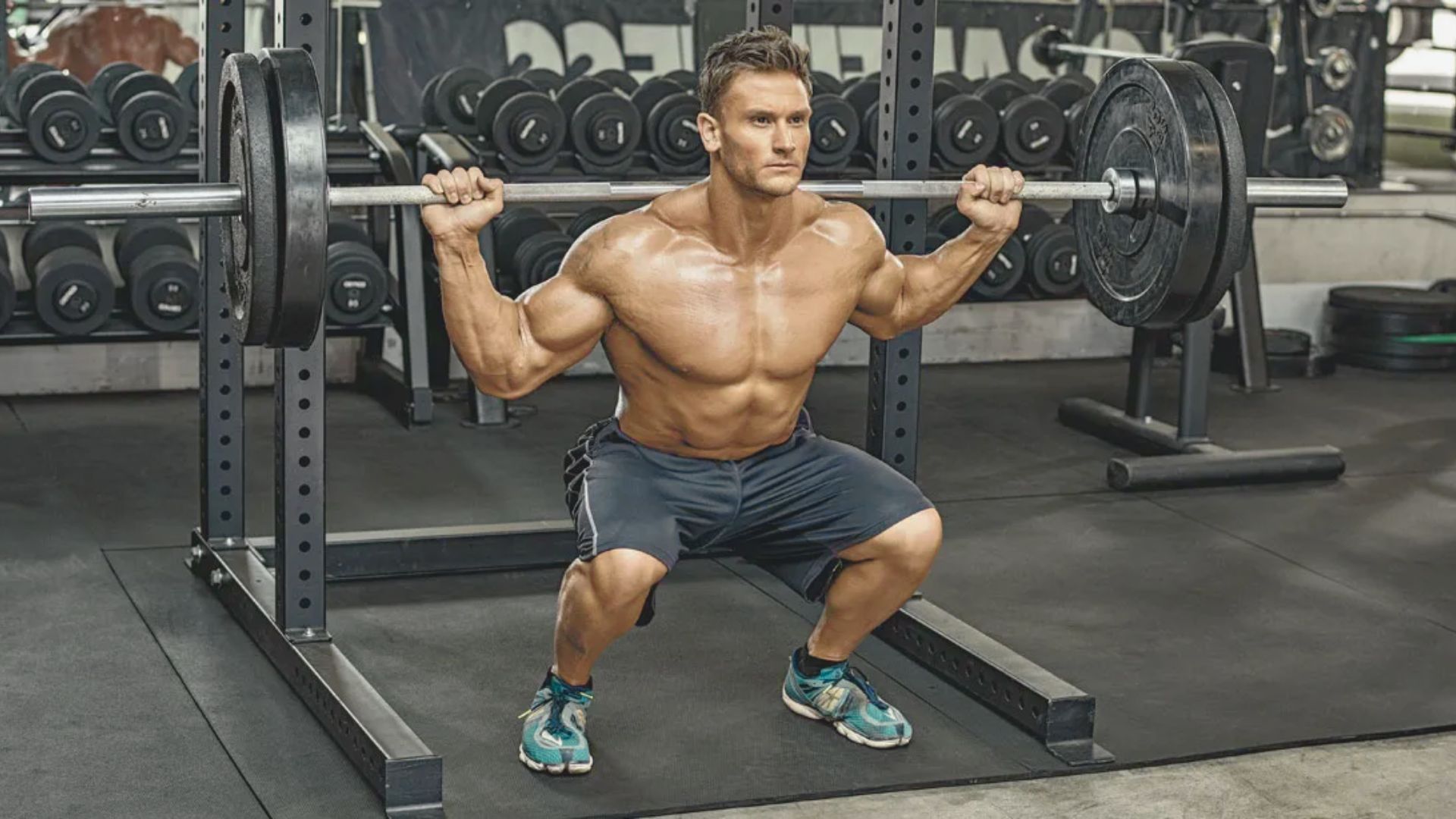 A man squats with a barbell on his shoulders in a gym, focusing on strength training and proper form.