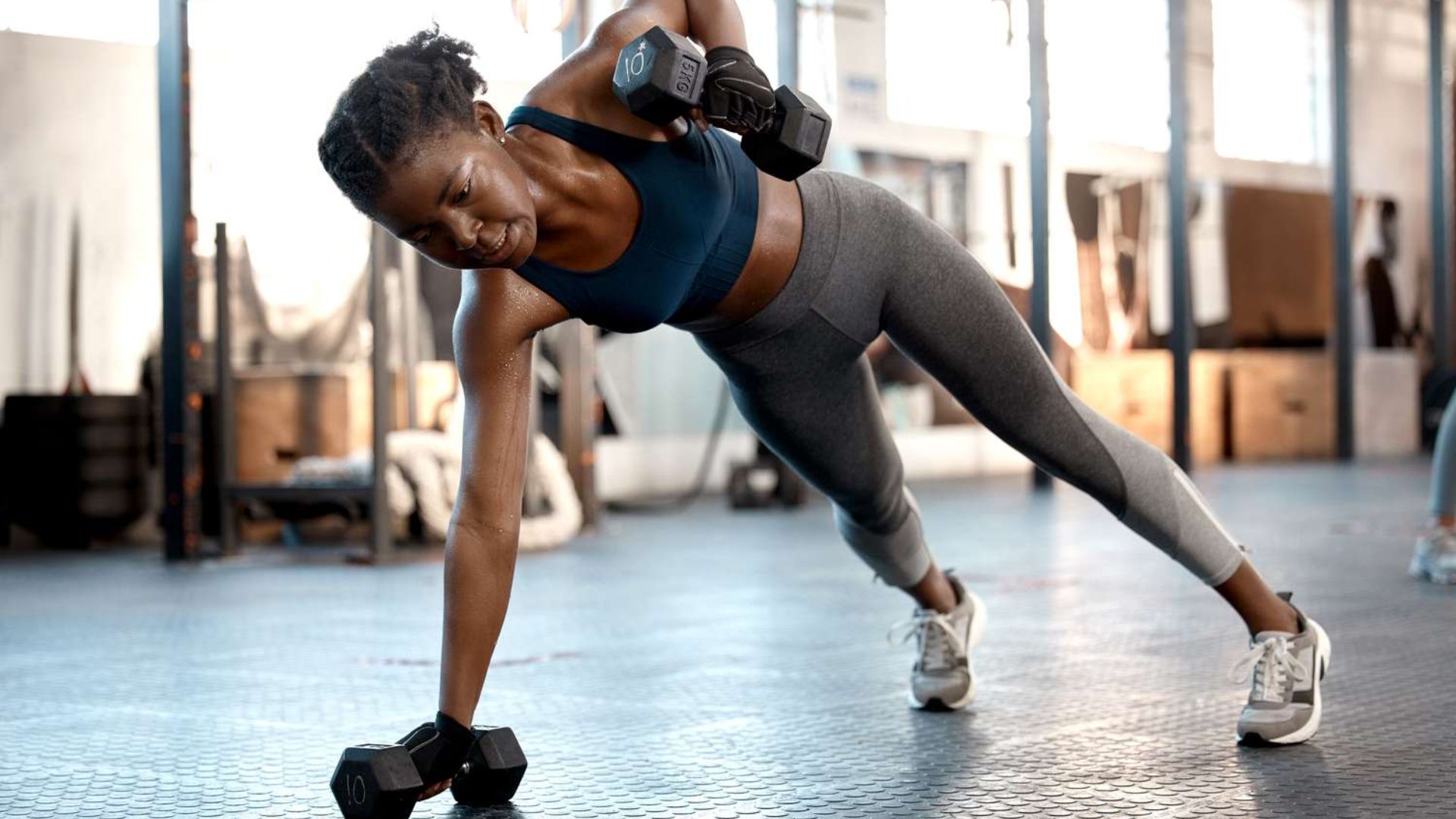 A woman performs a push-up while holding a dumbbell, demonstrating strength training for cardio and endurance.