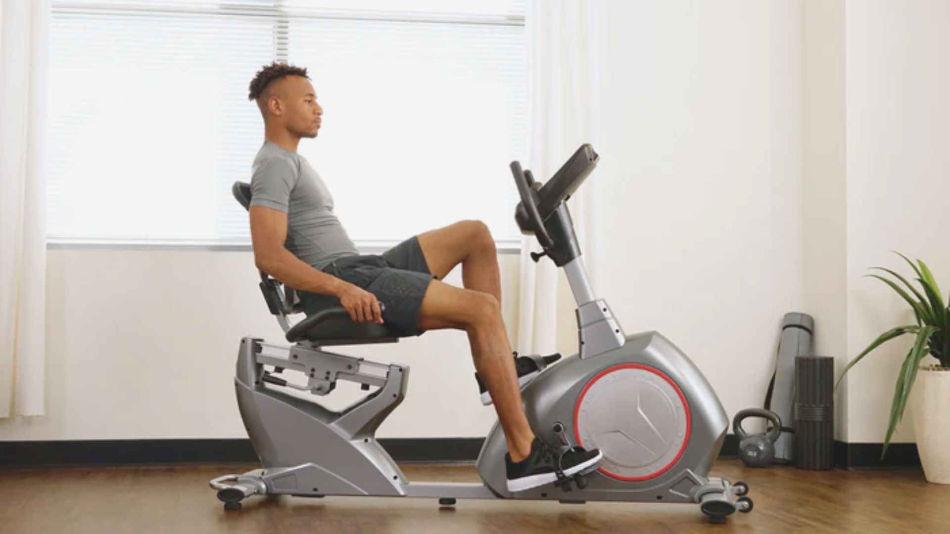 A man is seated on a stationary bike, focused on his workout in a well-lit exercise room.