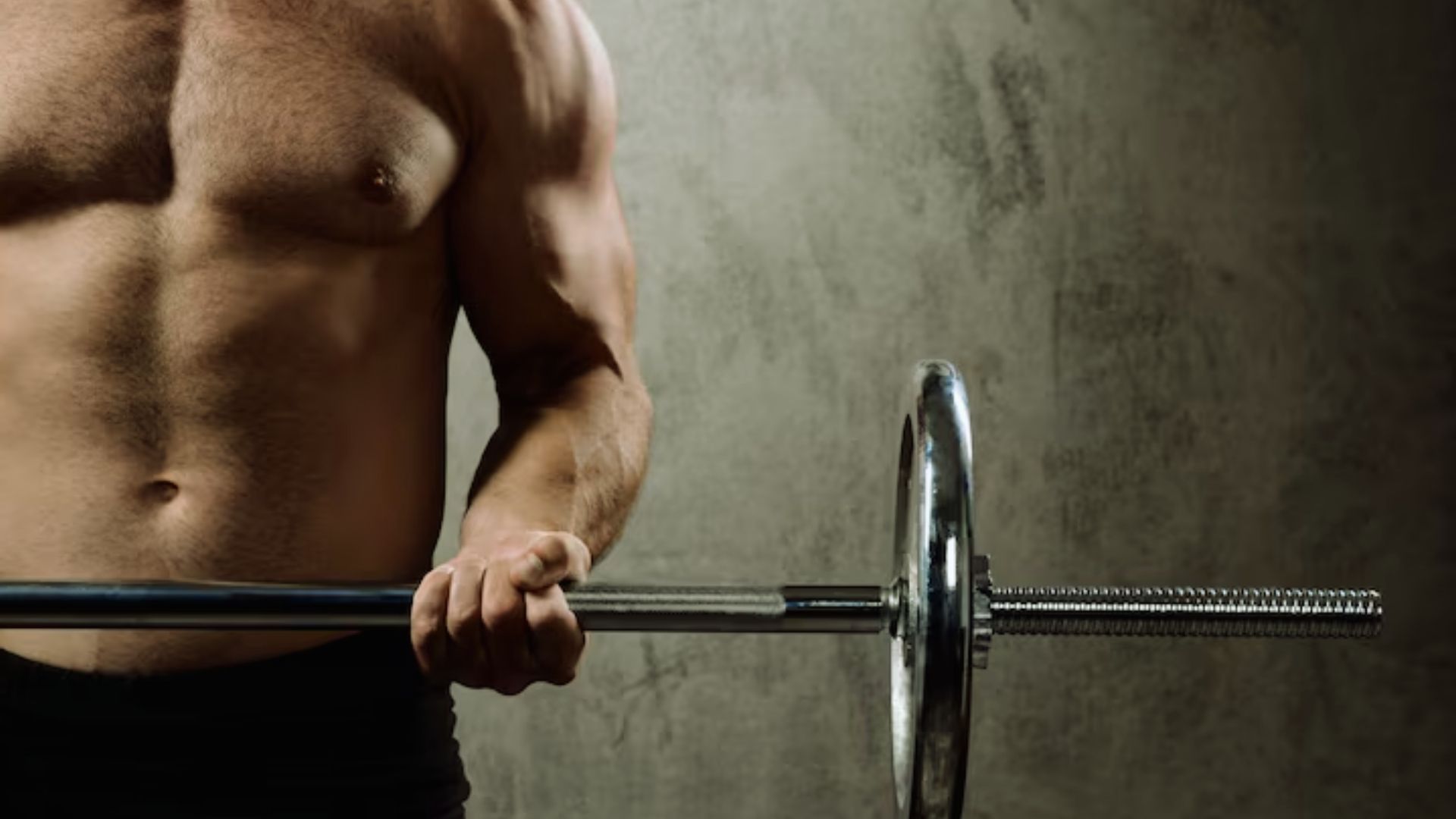 A shirtless man lifts a barbell, showcasing strength and focus in a gym setting.