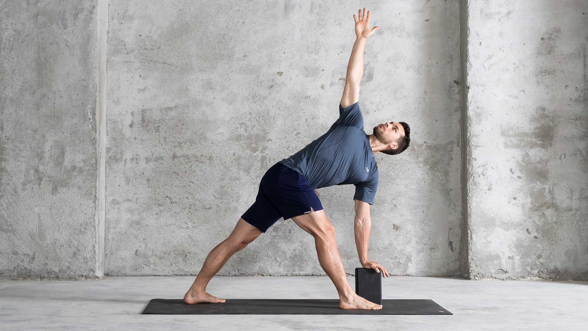 A man is engaged in a yoga pose on a black block, showcasing his balance and flexibility.