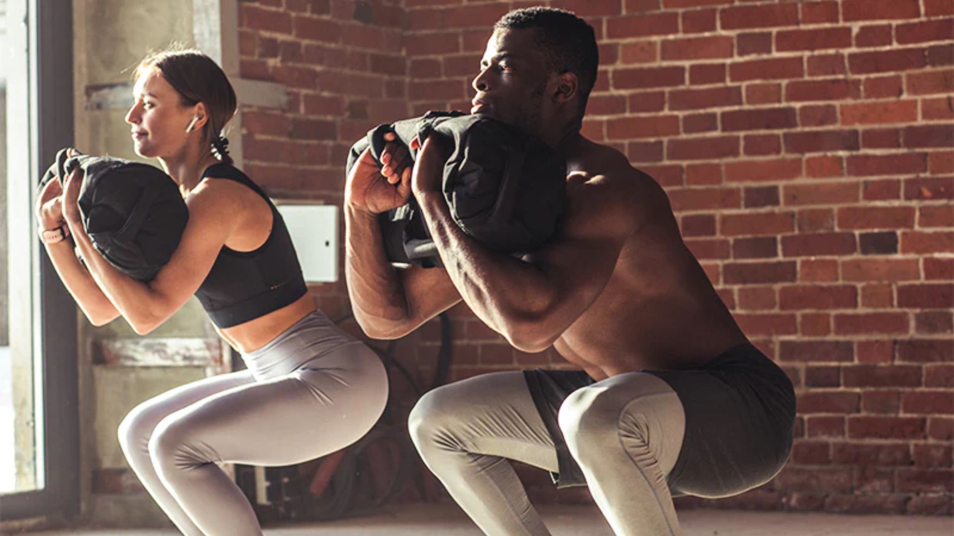 A man and woman performing squats in a gym, demonstrating proper exercise technique and teamwork.